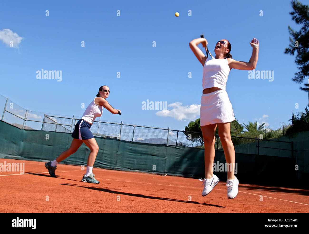 Due giovani sportivi tennis femminile giocatori avente un gioco di tennis al sole spagnolo. La corte è fatta di arancio brillante asfalto Foto Stock