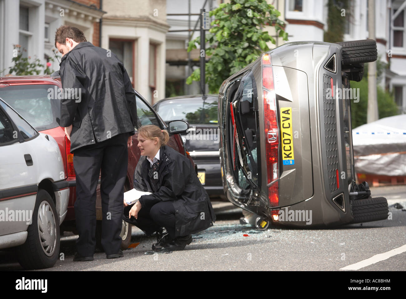 Gli ufficiali di polizia ispezionare il danno a una macchina parcheggiata dopo una Honda Civic si è schiantato durante una alta velocità di esercizio a Herne Hill, Londra. Foto Stock