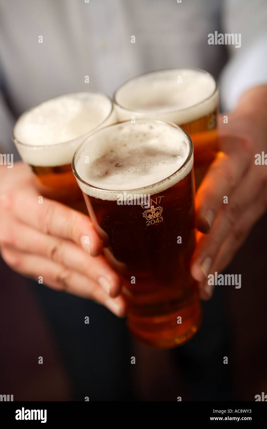 Portante tre pinte di birra lager tenuti insieme in un triangolo Foto Stock