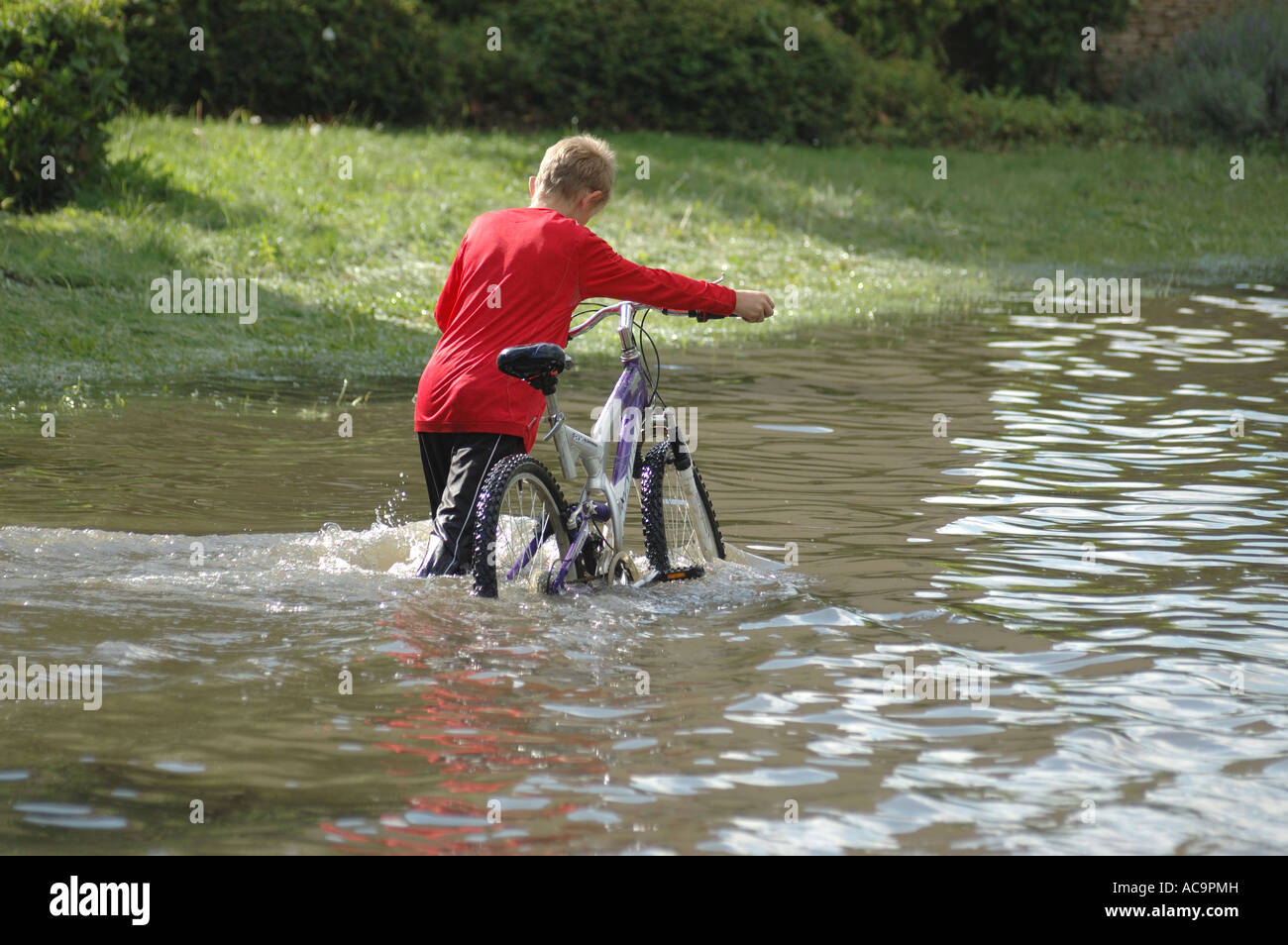 Ragazzo con una bicicletta in acqua di inondazione Foto Stock