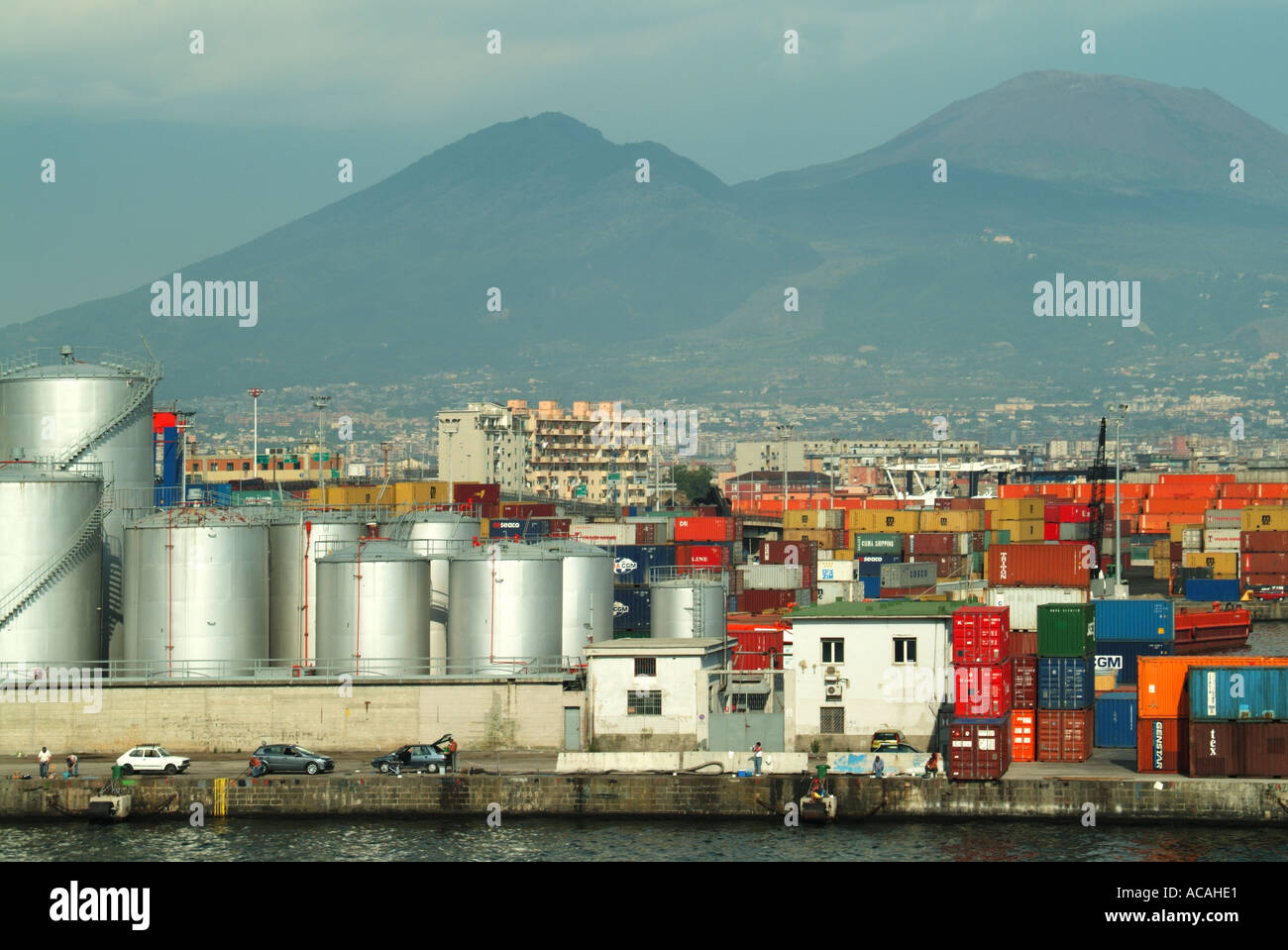 Napoli paesaggio industriale portuale contenitori stoccaggio serbatoi e gru oltre la nascita di spedizione vuota con persone che pescano dal molo accanto auto parcheggiate Foto Stock
