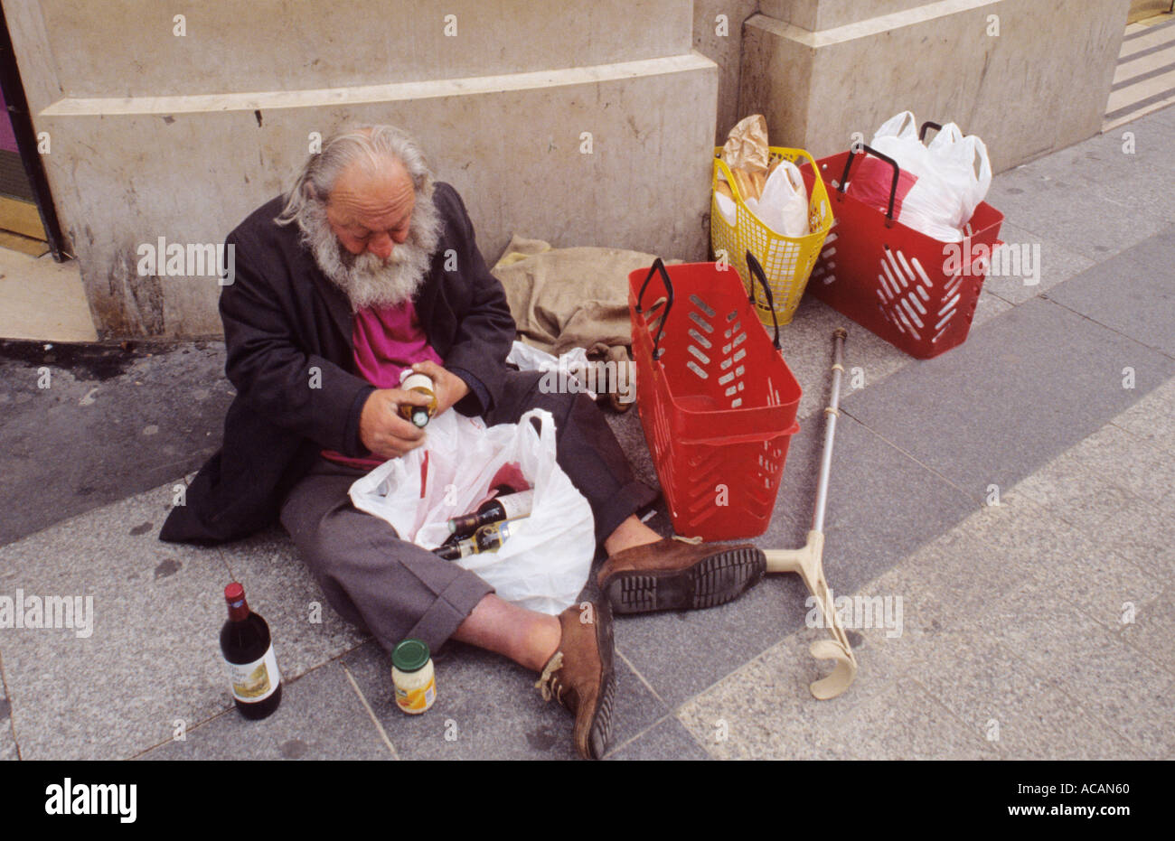 Alcolizzato senzatetto disabile anziano seduto sul marciapiede della città con bottiglie di vino nel centro della città. Foto Stock