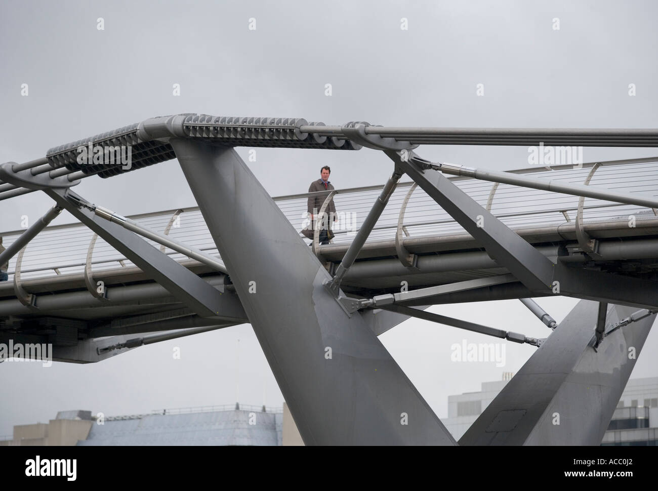 Un imprenditore passeggiate attraverso il Millennium Bridge sul fiume Tamigi a Londra in una giornata di vento Foto Stock