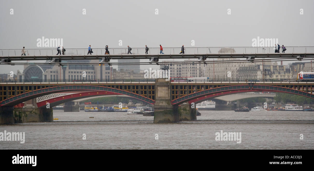 Passeggiate pedonali attraverso il Millennium Bridge sul fiume Tamigi a Londra Inghilterra. Il famoso Blackfriars bridge nella parte posteriore Foto Stock