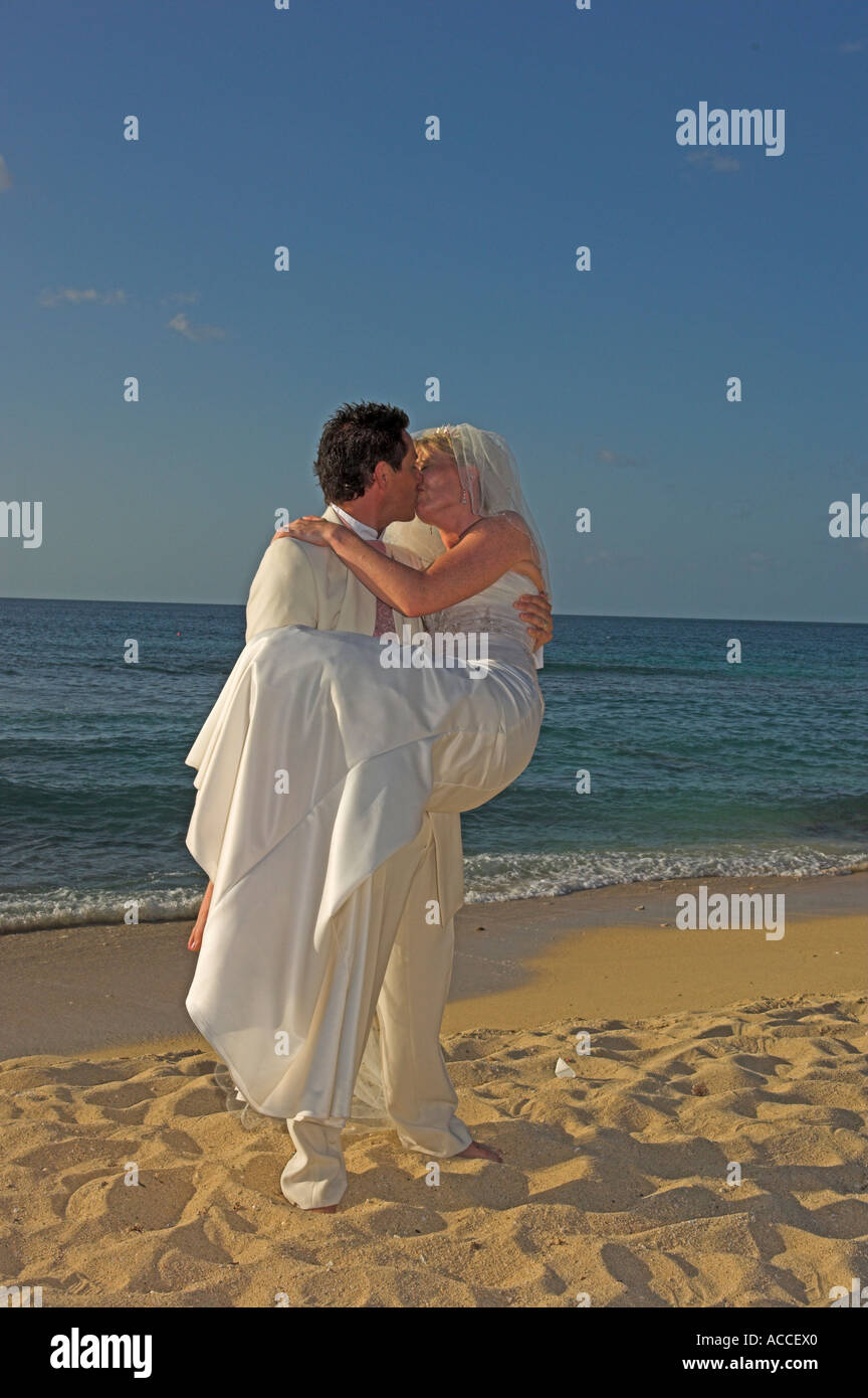 Lo sposo che trasportano sposa caldo sulla spiaggia di sabbia dorata nel tardo pomeriggio Foto Stock