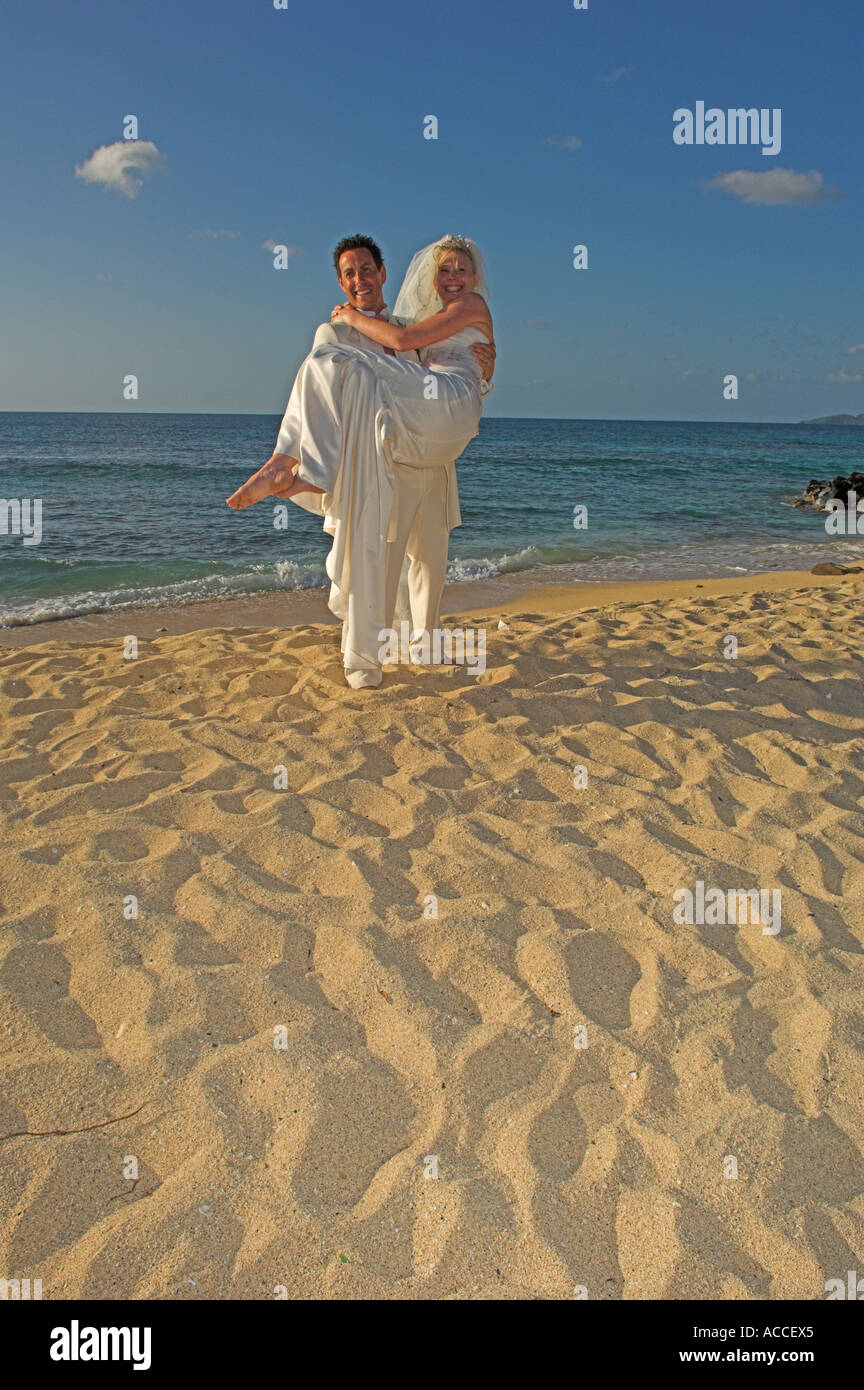 Lo sposo che trasportano sposa caldo sulla spiaggia di sabbia dorata nel tardo pomeriggio Foto Stock