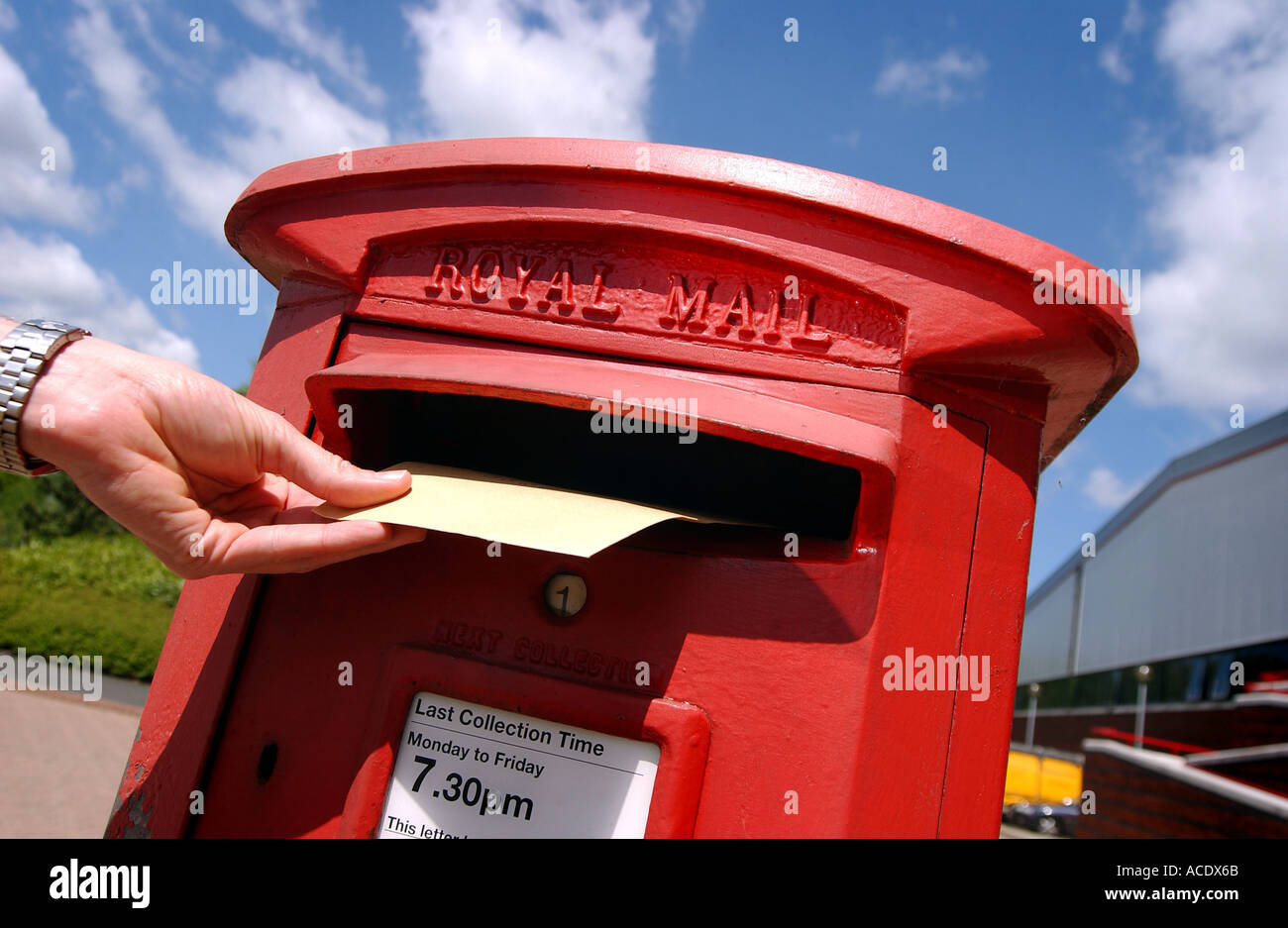 Una mano spedire una lettera in un royal mail postbox in una giornata di sole Foto Stock