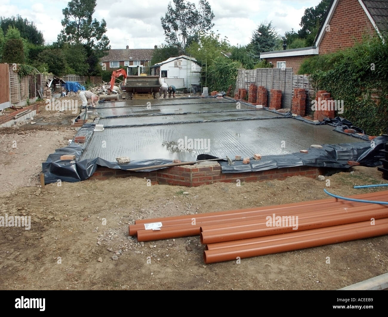 Operaio e i lavori in corso in materia di recente consegnato wet ready mix concrete versare alla sottostruttura soletta alla nuova casa in costruzione England Regno Unito Foto Stock