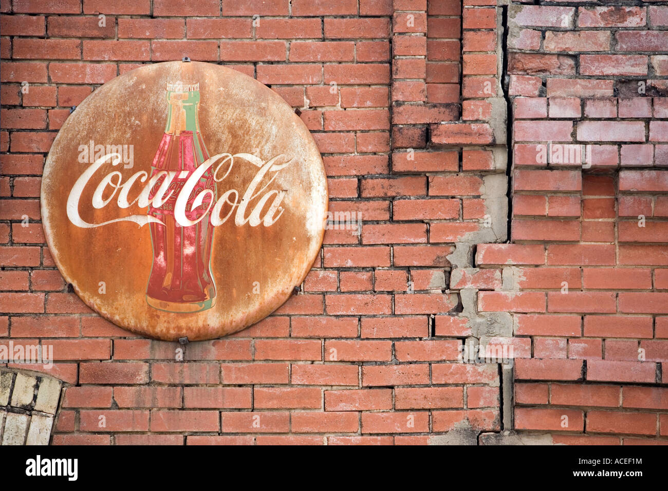 Coca Cola segno rotondo sul vecchio edificio in mattoni sbiaditi e arrugginito orizzontale in acciaio Foto Stock