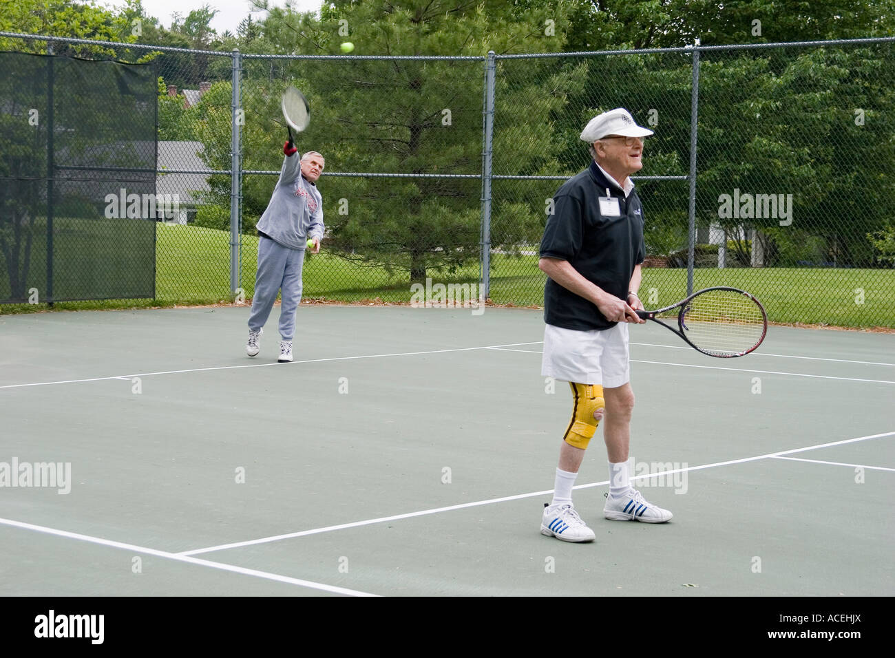 Anziani pensionati uomini giocare un doppio gioco di tennis come parte di un senior Olympics torneo a un proseguimento della cura facility Foto Stock