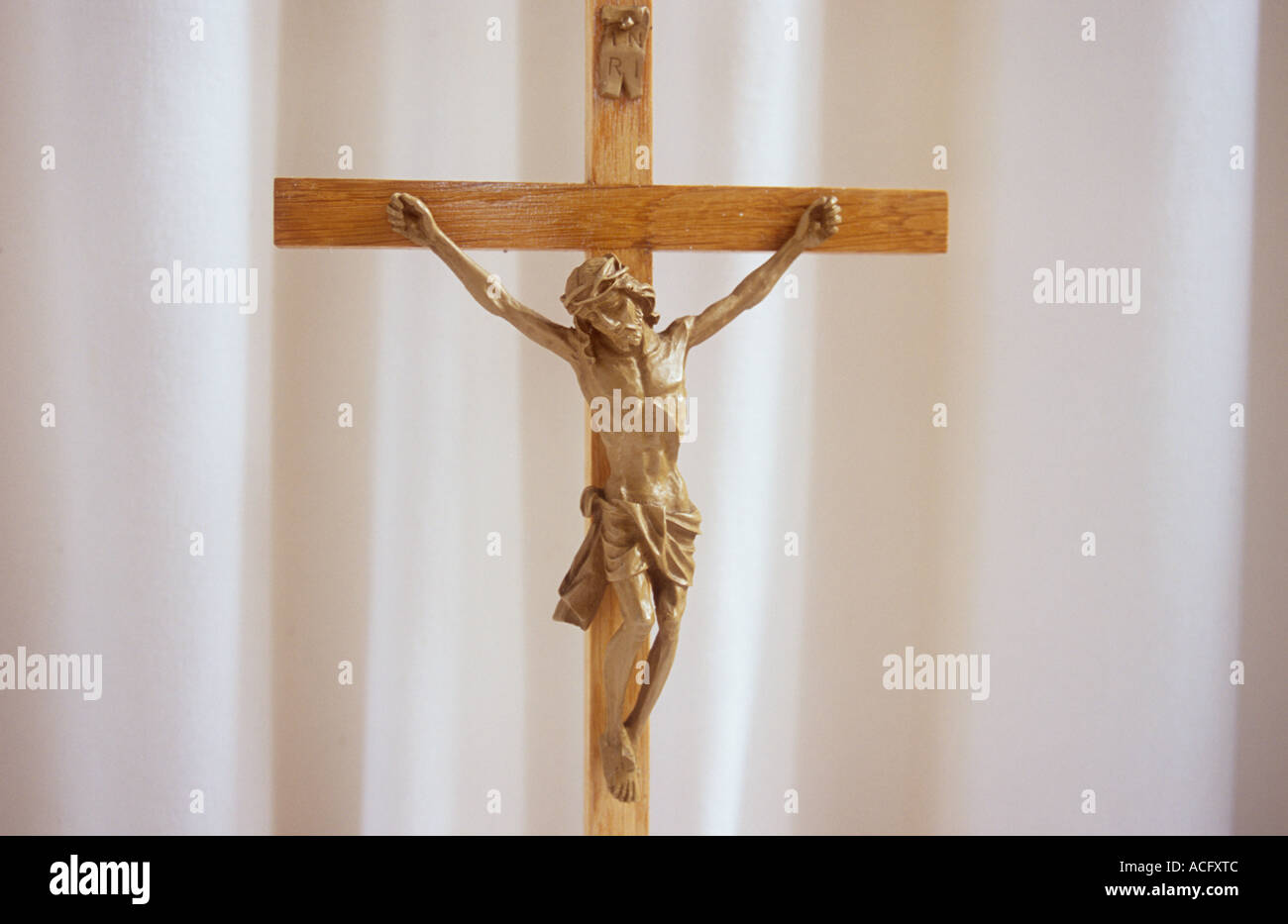 Close up di Gesù Cristo su un crocifisso in legno di fronte le pieghe di un pallido bianco crema cortina o un telo Foto Stock