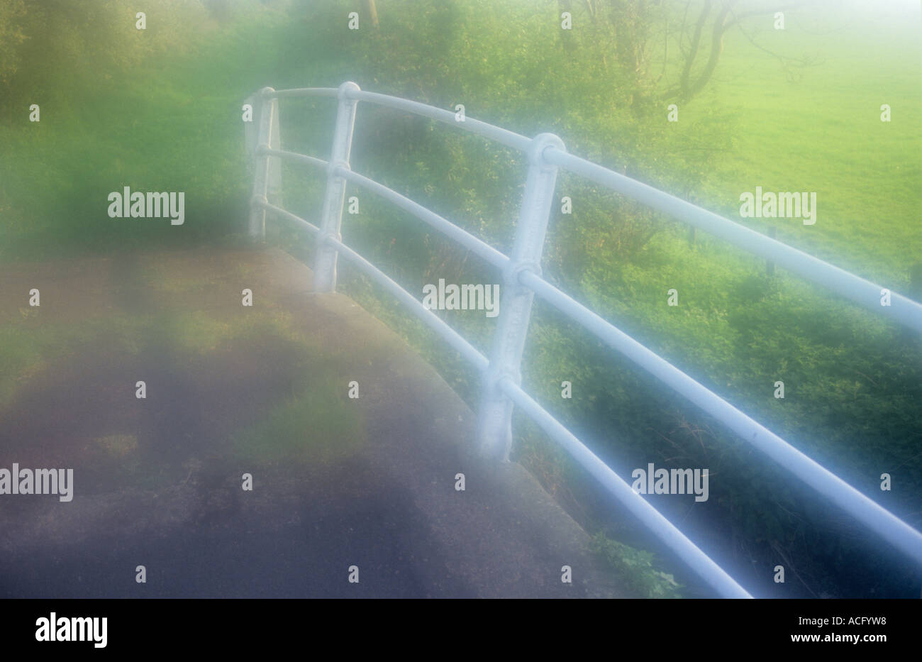 Vista atmosferica di ringhiere in bianco con calcestruzzo hump backed ponte sul torrente con erba ortica boccole nella calda luce della molla Foto Stock