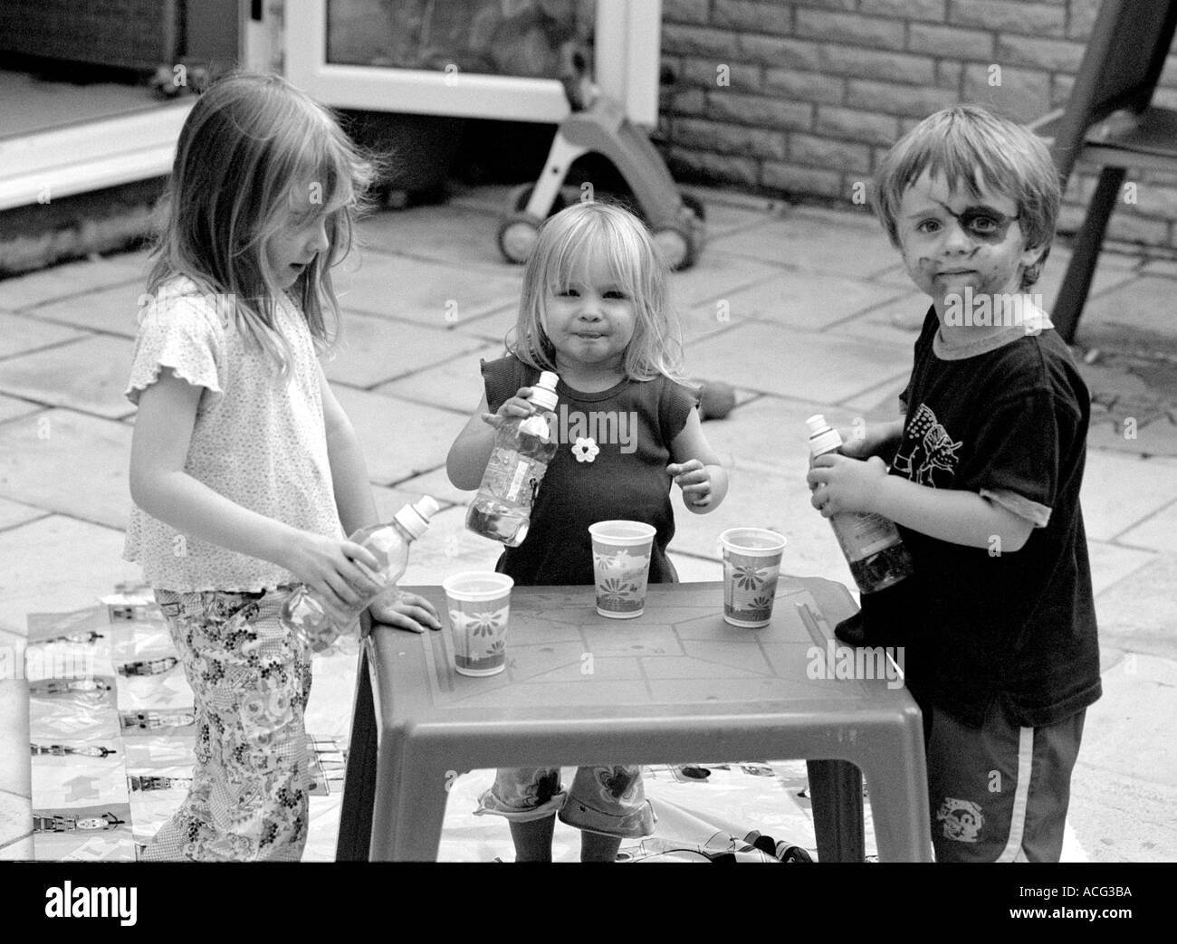 Tre bambini mescita di bevande al tavolo in plastica Foto Stock