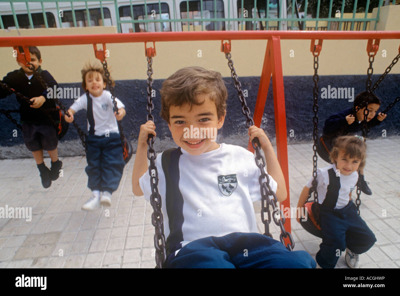 I bambini delle scuole infantili godono di giocare sul parco giochi della scuola altalene Foto Stock