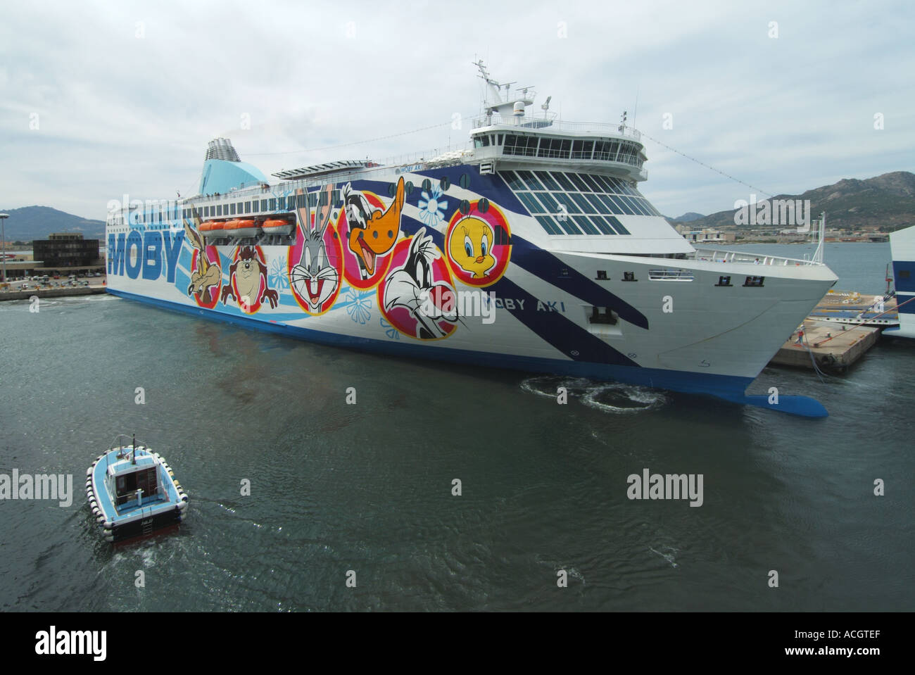 Olbia Sardina porta linee Moby Aki grafica di traghetti che raffigurano i personaggi dei cartoni animati docking assistita da utilizzando spintore laterale Foto Stock