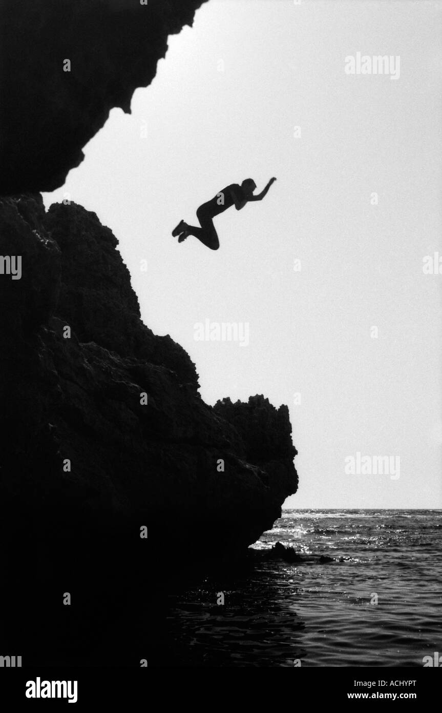 Immagine in bianco e nero di una persona che salta da una roccia nell'oceano Foto Stock