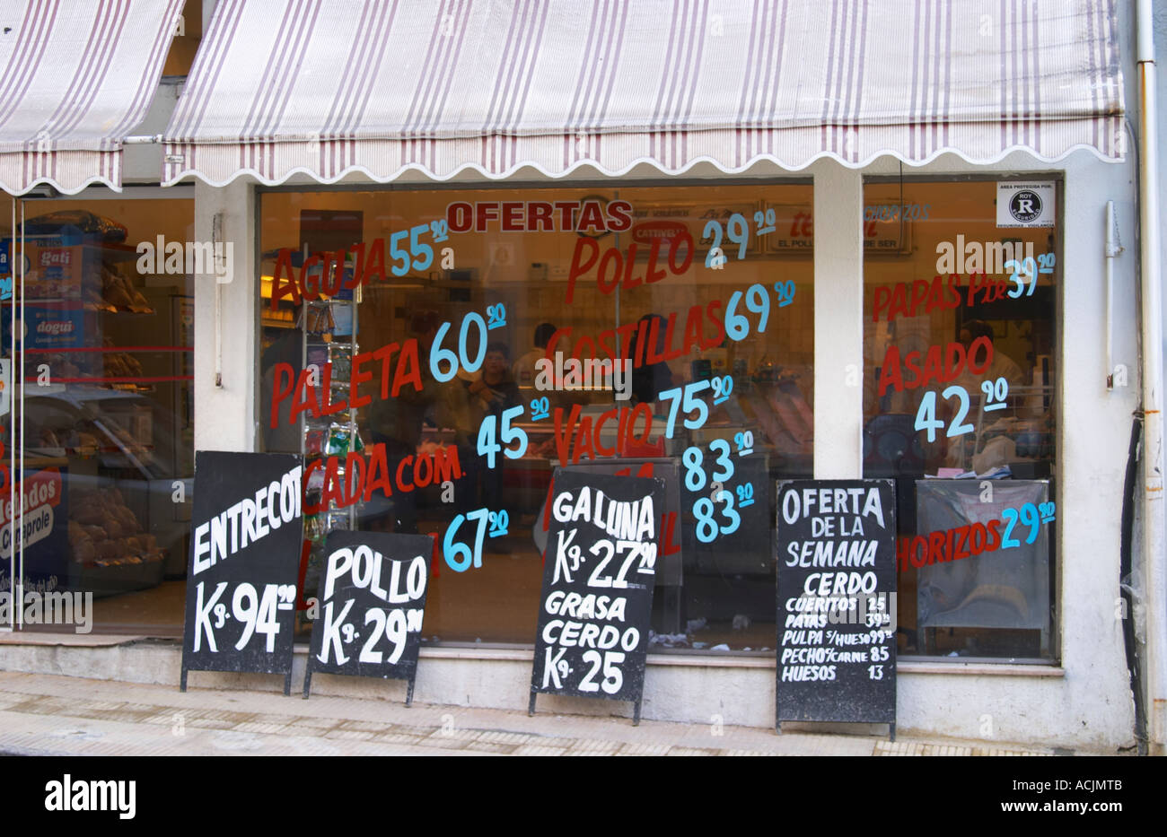 Una macelleria la vendita di carne e pollame pollo, con un sacco di pubblicità sulla finestra dipinte in rosso e blu lettere e sulle schede di gesso in bianco in piedi sul marciapiede. Montevideo, Uruguay Sud America Foto Stock