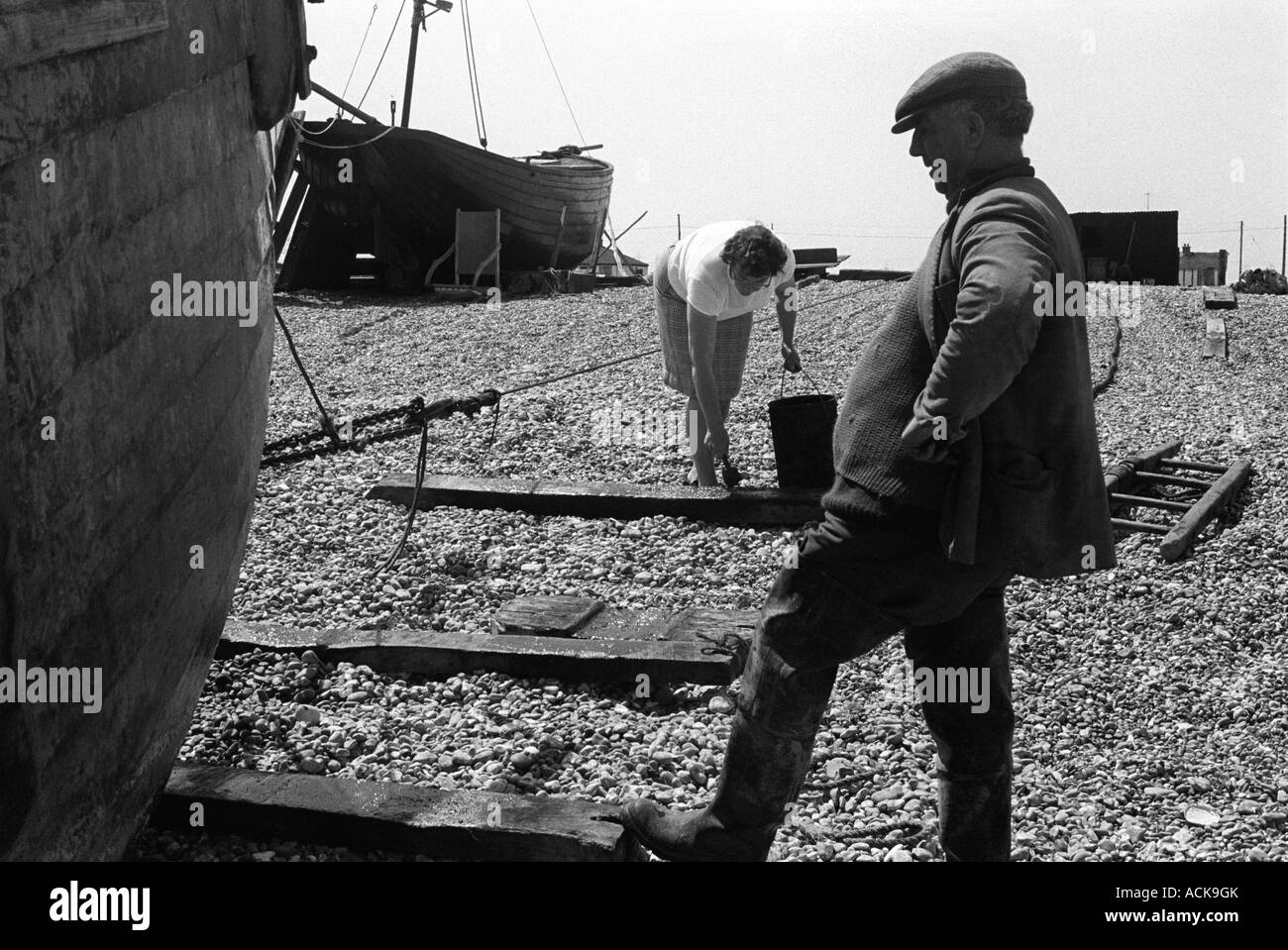 Fisherman e moglie Dungeness Kent anni '1960 Regno Unito. Donna pescatrice costiera che dipinge creosoto su piste di legno, in modo che le barche possano essere trascinate fino alla spiaggia 1969. Foto Stock