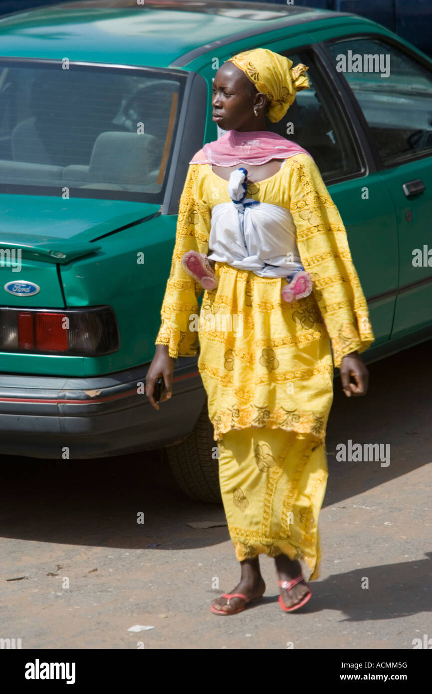 Piedi del bambino in sling sotto le armi della donna che cammina in giallo abiti tradizionali del mercato Serekunda Gambia Foto Stock