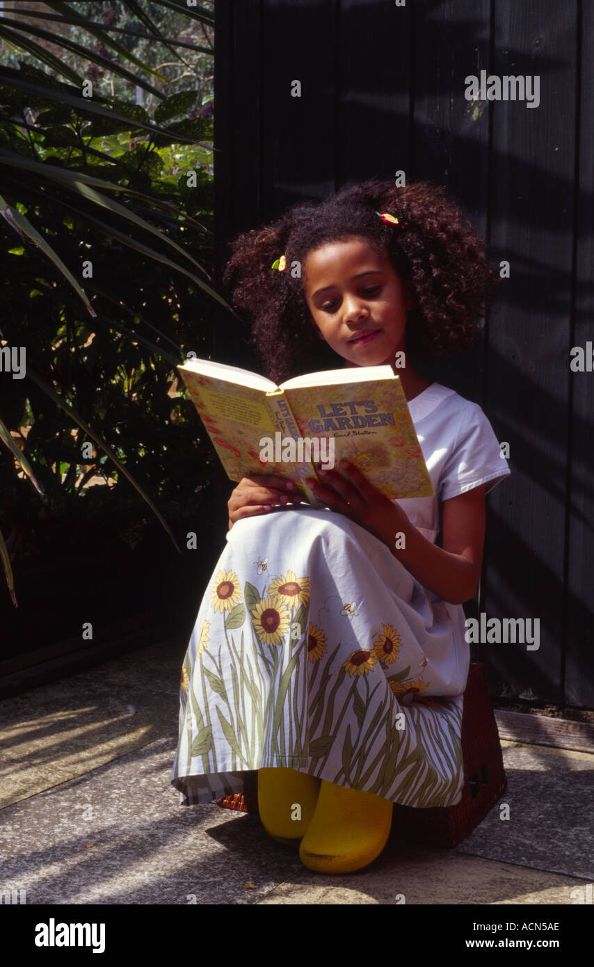 Bambina indossa un abito e zoccoli di giardinaggio seduto fuori da un  capannone leggendo un libro di Enid Chelmsford Foto stock - Alamy