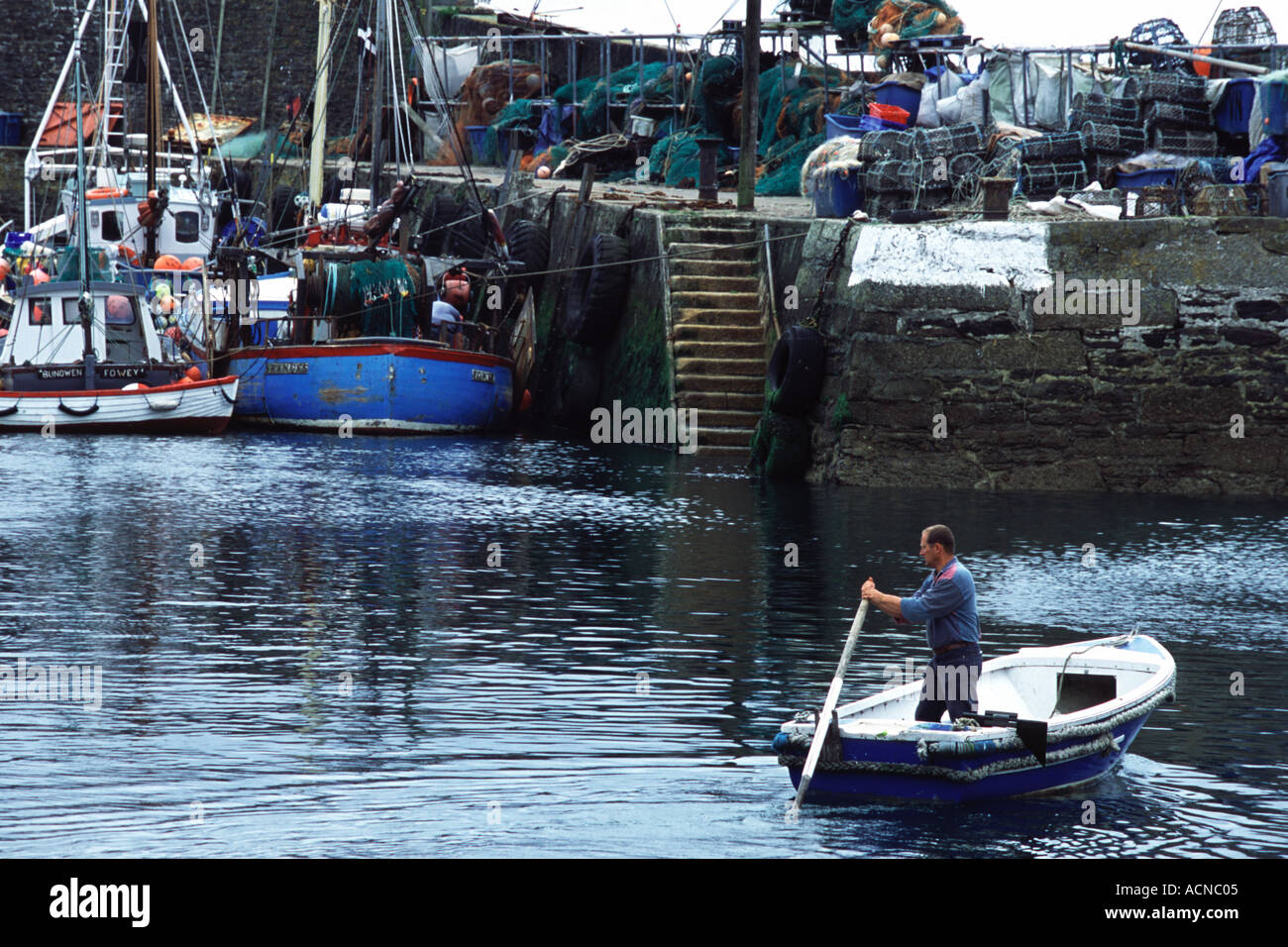 Un locale della Cornovaglia fisherman remi il suo piccolo tender verso il braccio del porto Foto Stock