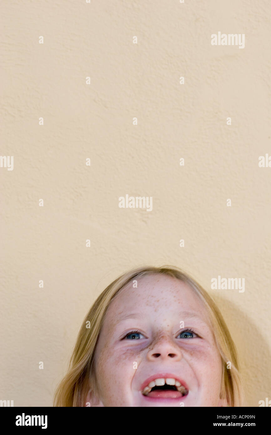 Viso della ragazza bionda modello, età nove, ridendo come si guarda in alto Foto Stock