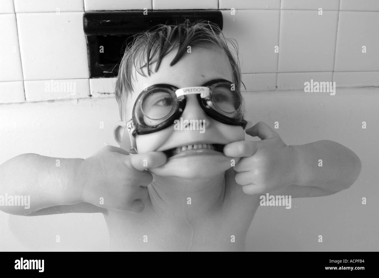 Piccolo Ragazzo in vasca nuotatori che indossa gli occhiali di protezione rendendo divertente volto sorridente ridere umorismo umorismo vita familiare Foto Stock