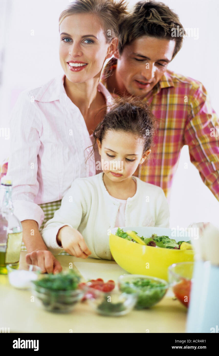 I genitori a guardare la figlia (6-7) la preparazione di insalata Foto Stock