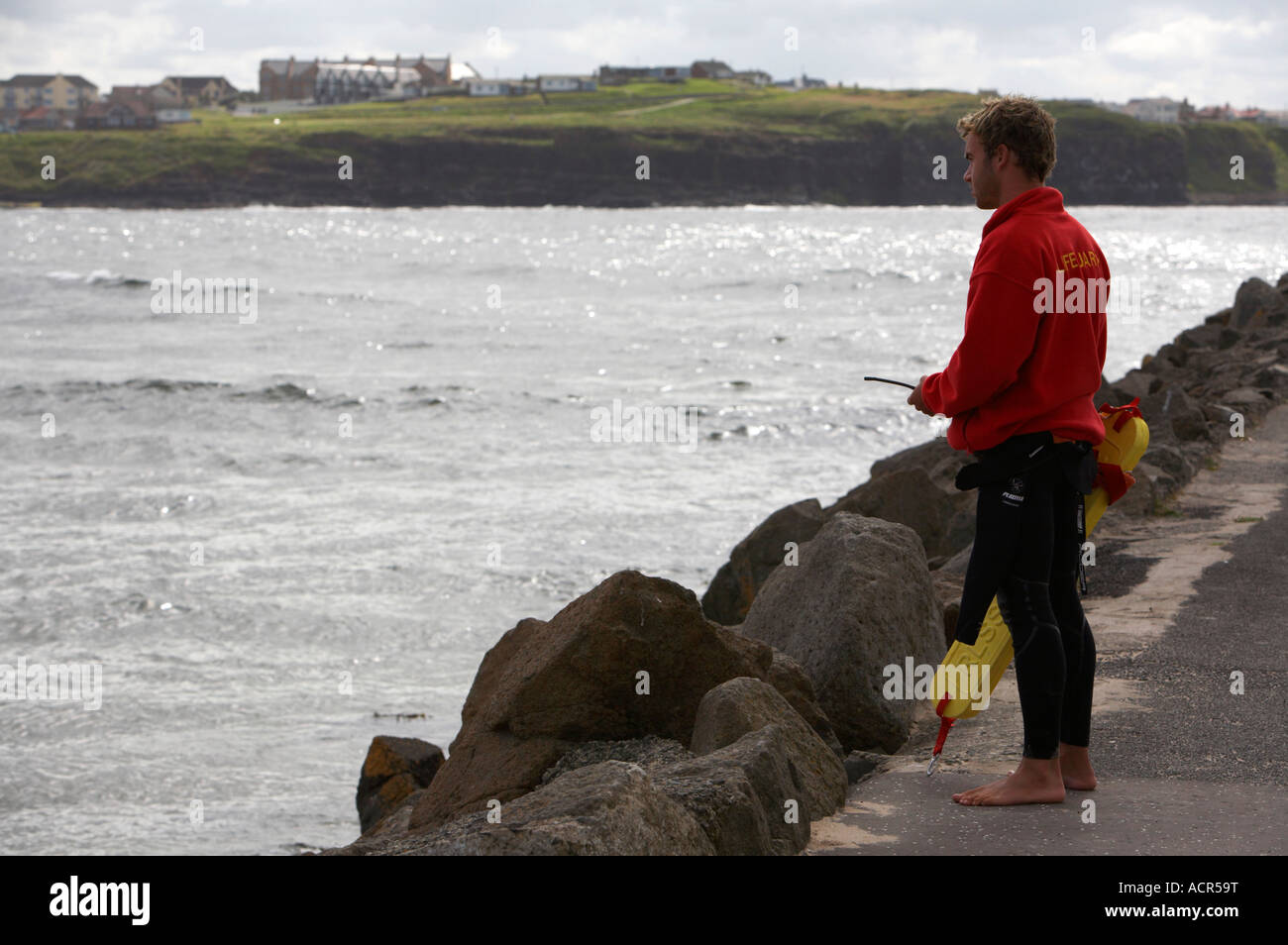 Surf maschio bagnino di salvataggio a guardare oltre la spiaggia a Portrush west strand con radio e flottazione aiuto a portata di mano Foto Stock