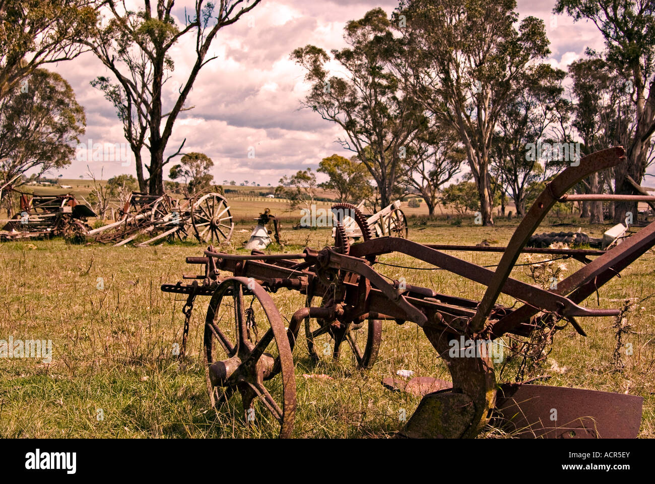 Un vecchio arrugginimento cavallo aratro siede nel paddock di fattoria circondata da altre apparecchiature rotto Foto Stock