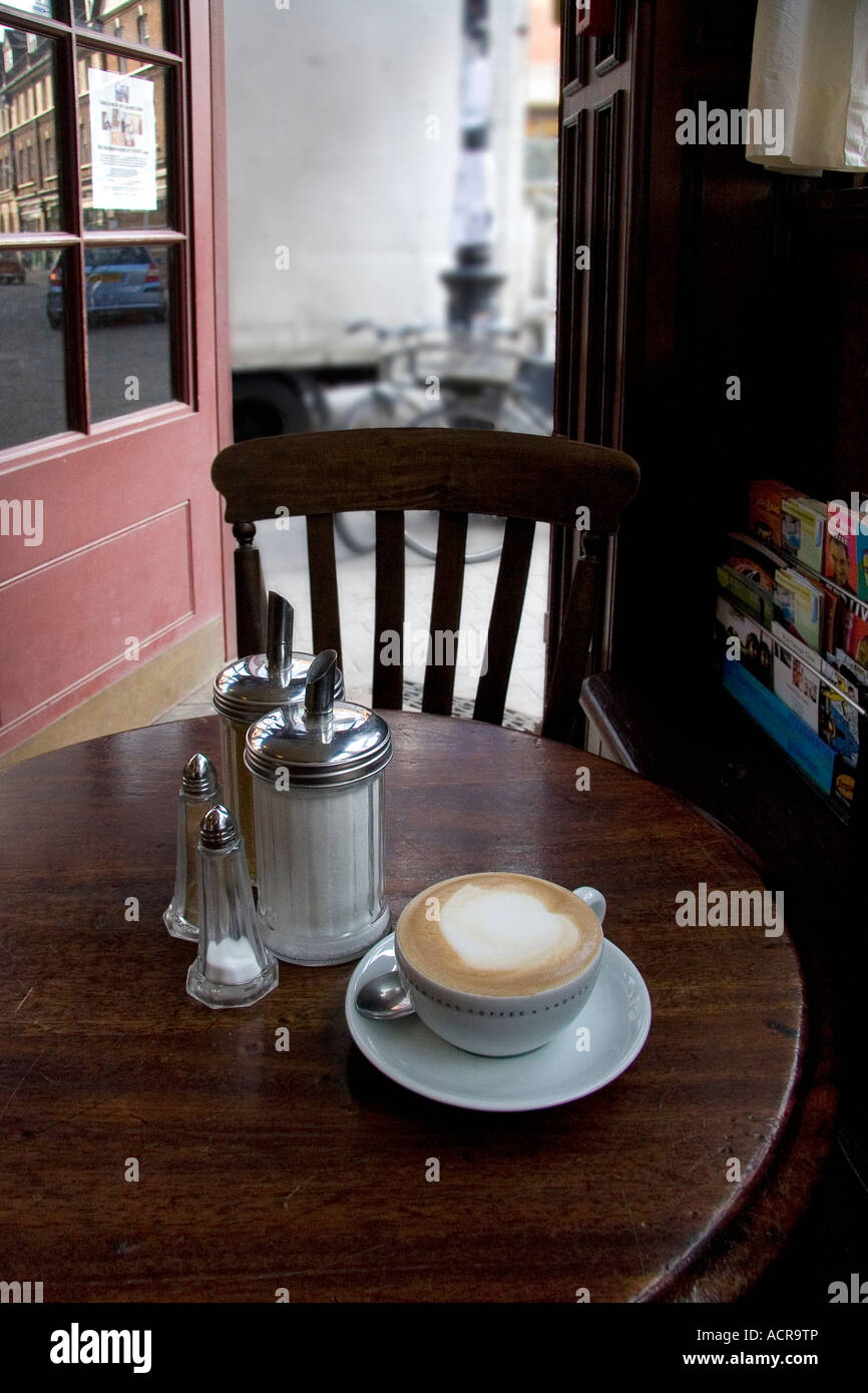 Un cappuccino caffè su di un tavolo di legno con lo zucchero e il sale e il pepe in contenitori in un caffè di Spitalfields a Londra REGNO UNITO Foto Stock