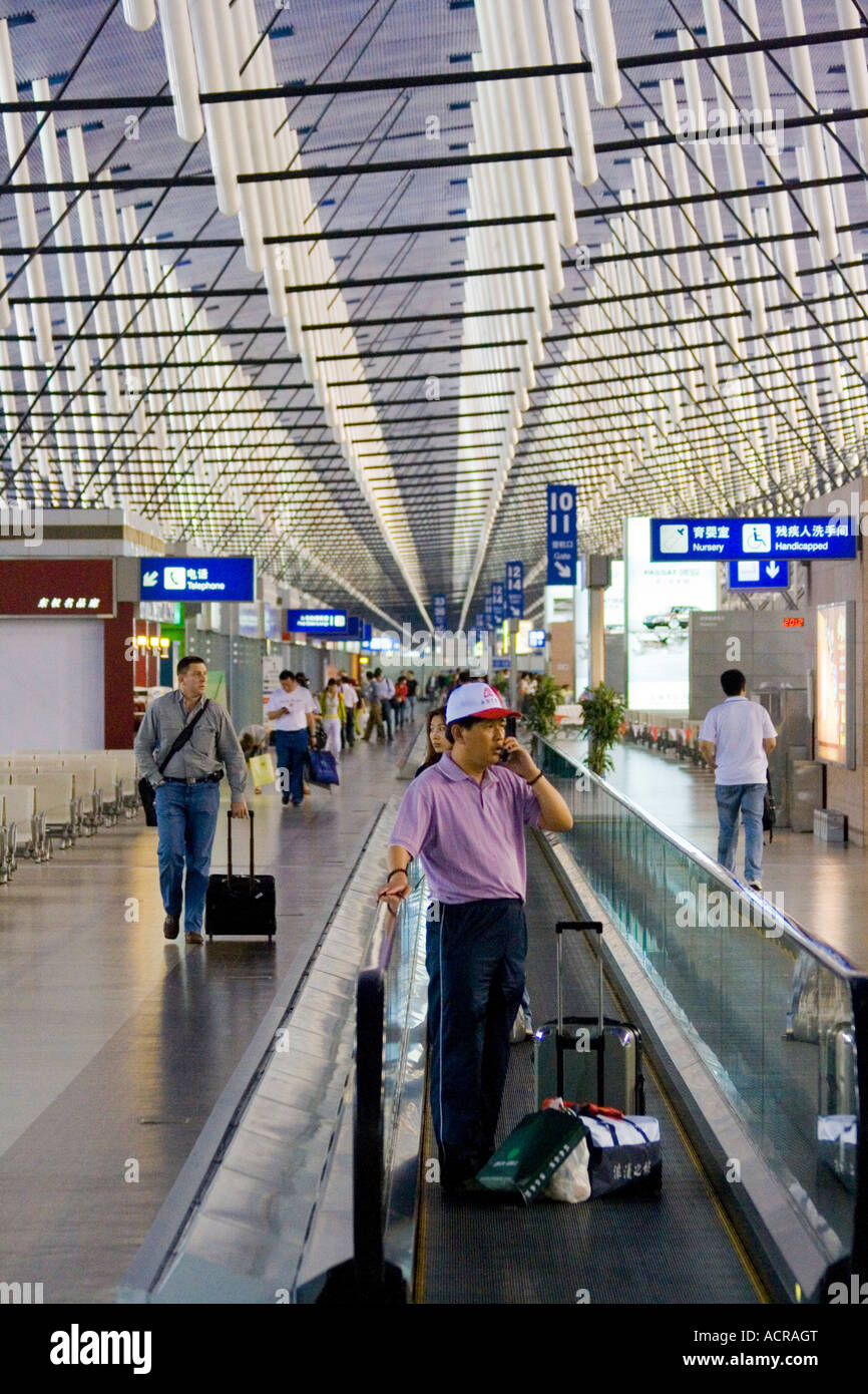 Uomo cinese sul tapis roulant parlando al telefono cellulare PVG Aeroporto Internazionale di Pudong Shanghai in Cina Foto Stock