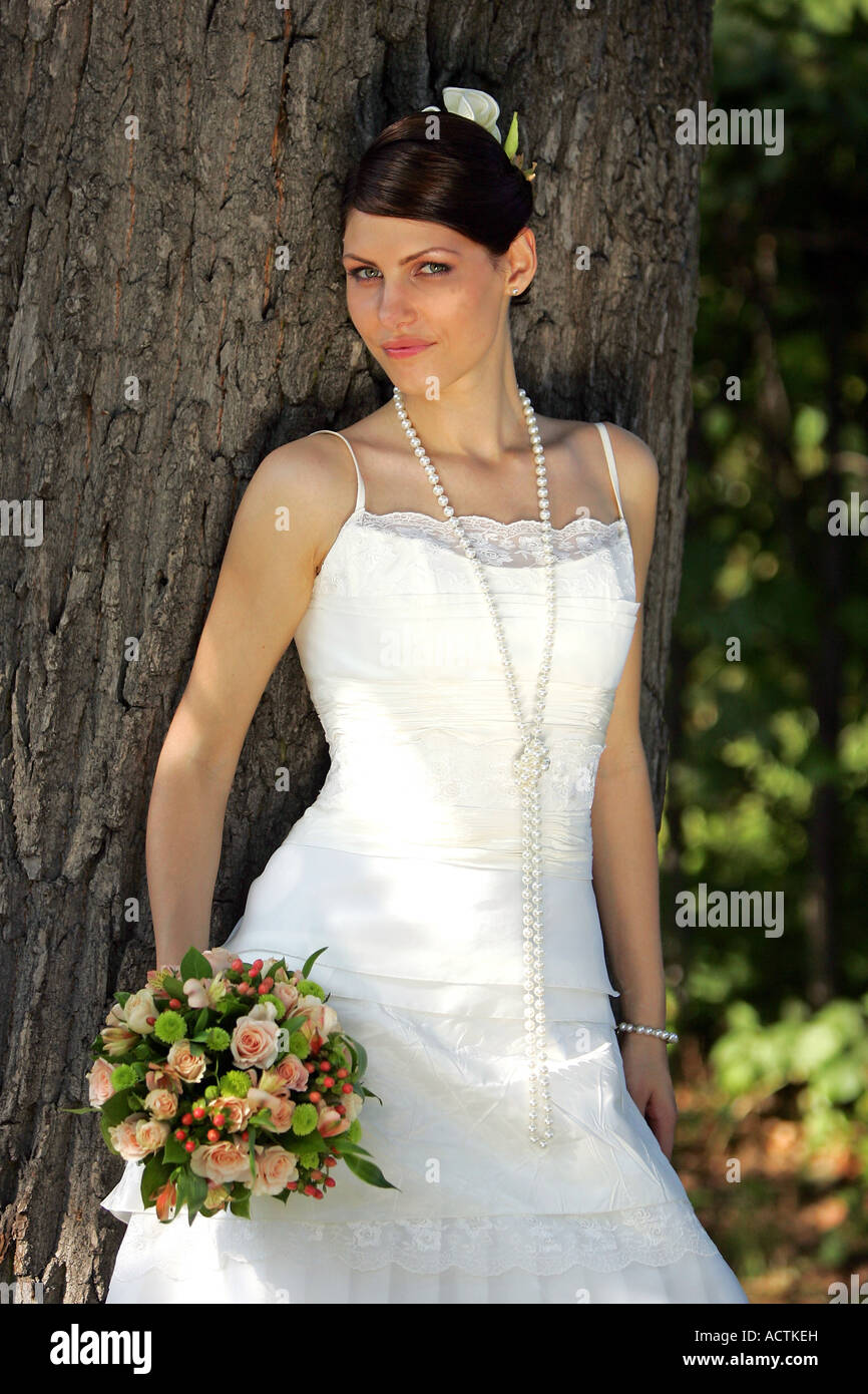 Ritratto di una sposa si fermò accanto ad albero con bouquet sorridente Foto Stock