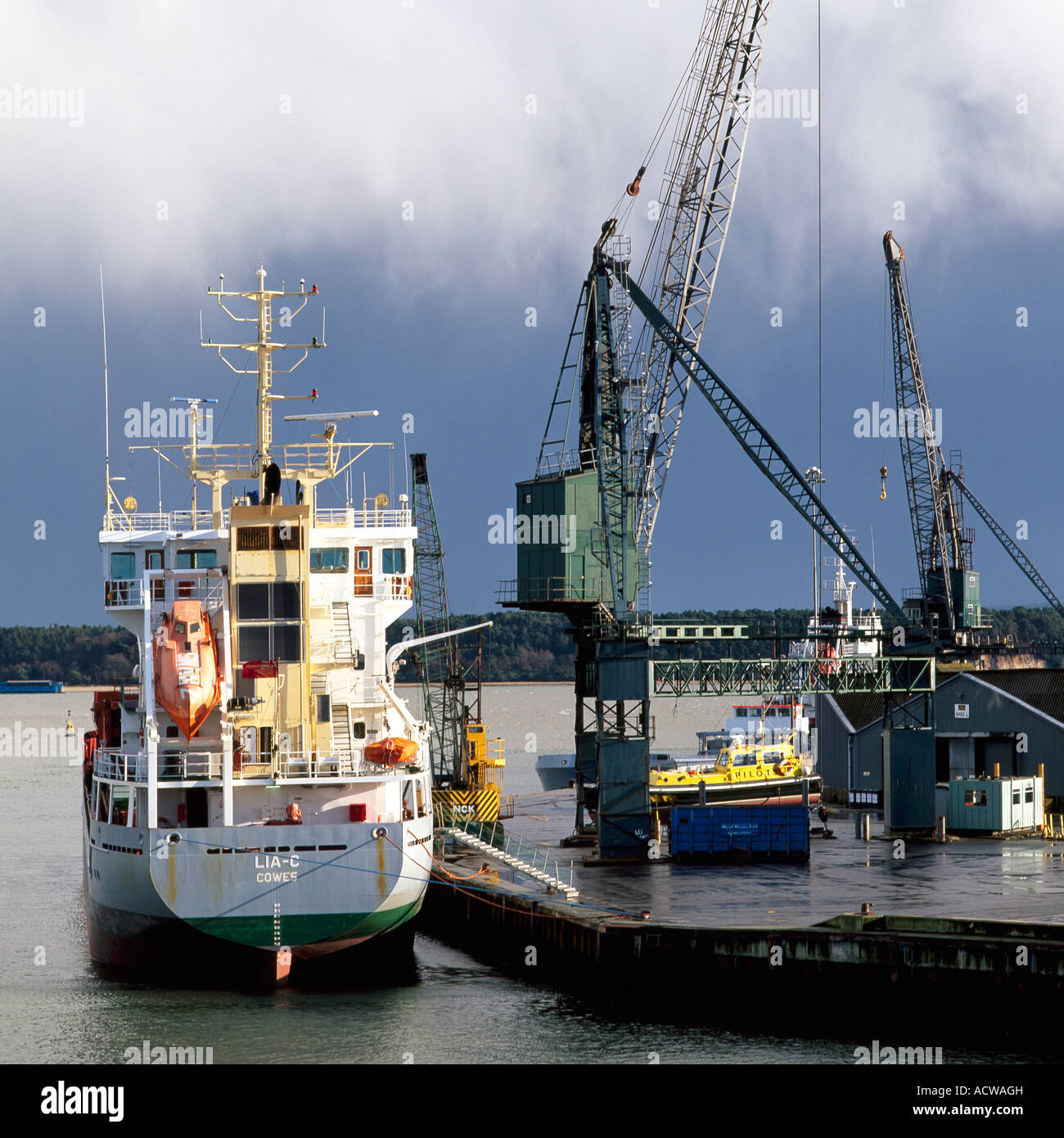 Nave da carico nel porto sotto nuvole temporalesche a fianco di una banchina di carico o lo scarico di merci per le importazioni o le esportazioni commerciali di Business Foto Stock