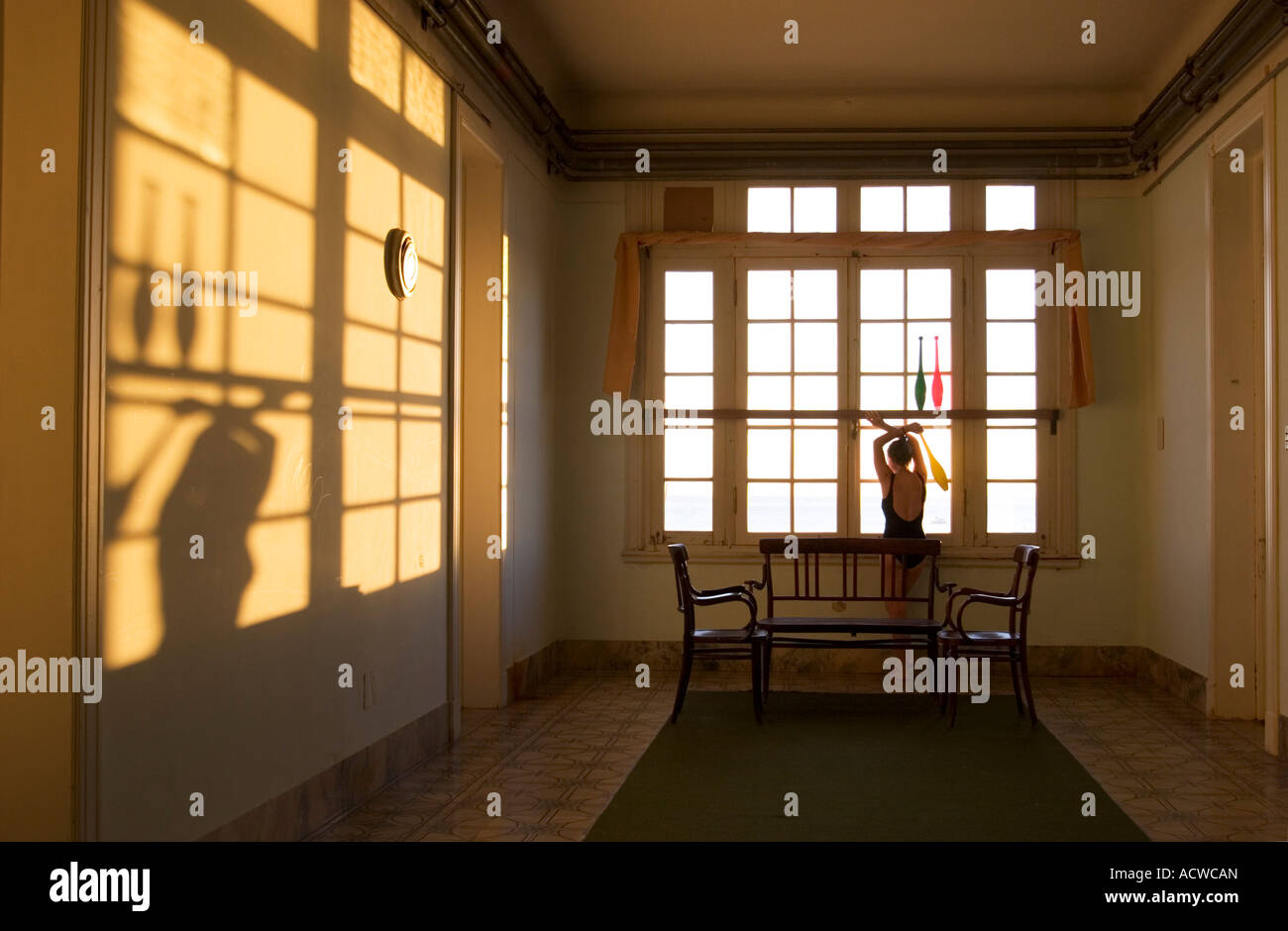 Donna con club di giocoleria di guardare attraverso una finestra con lunghe ombre al tramonto Foto Stock