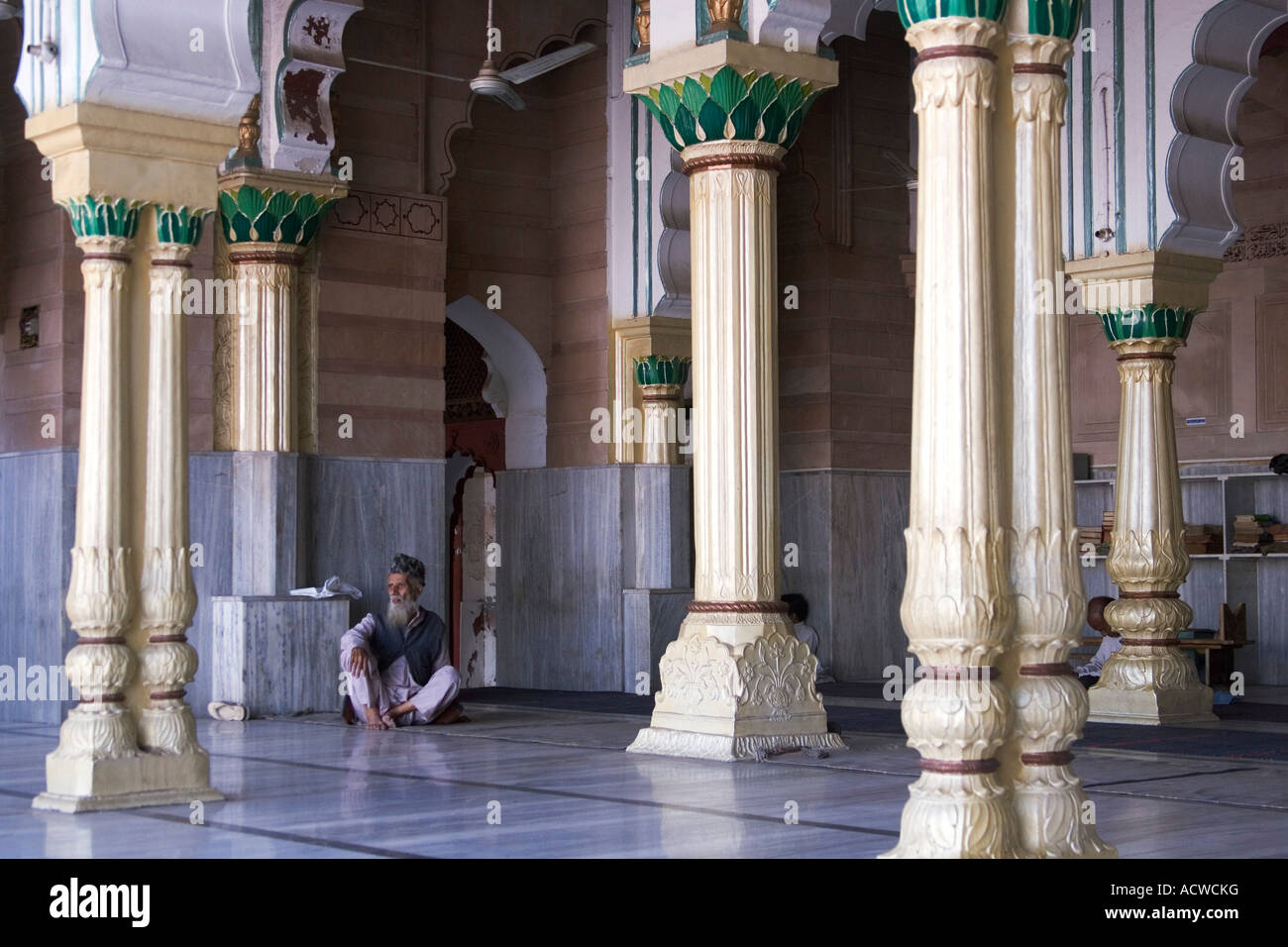Uomo seduto tra le colonne di una moschea India Delhi Foto Stock