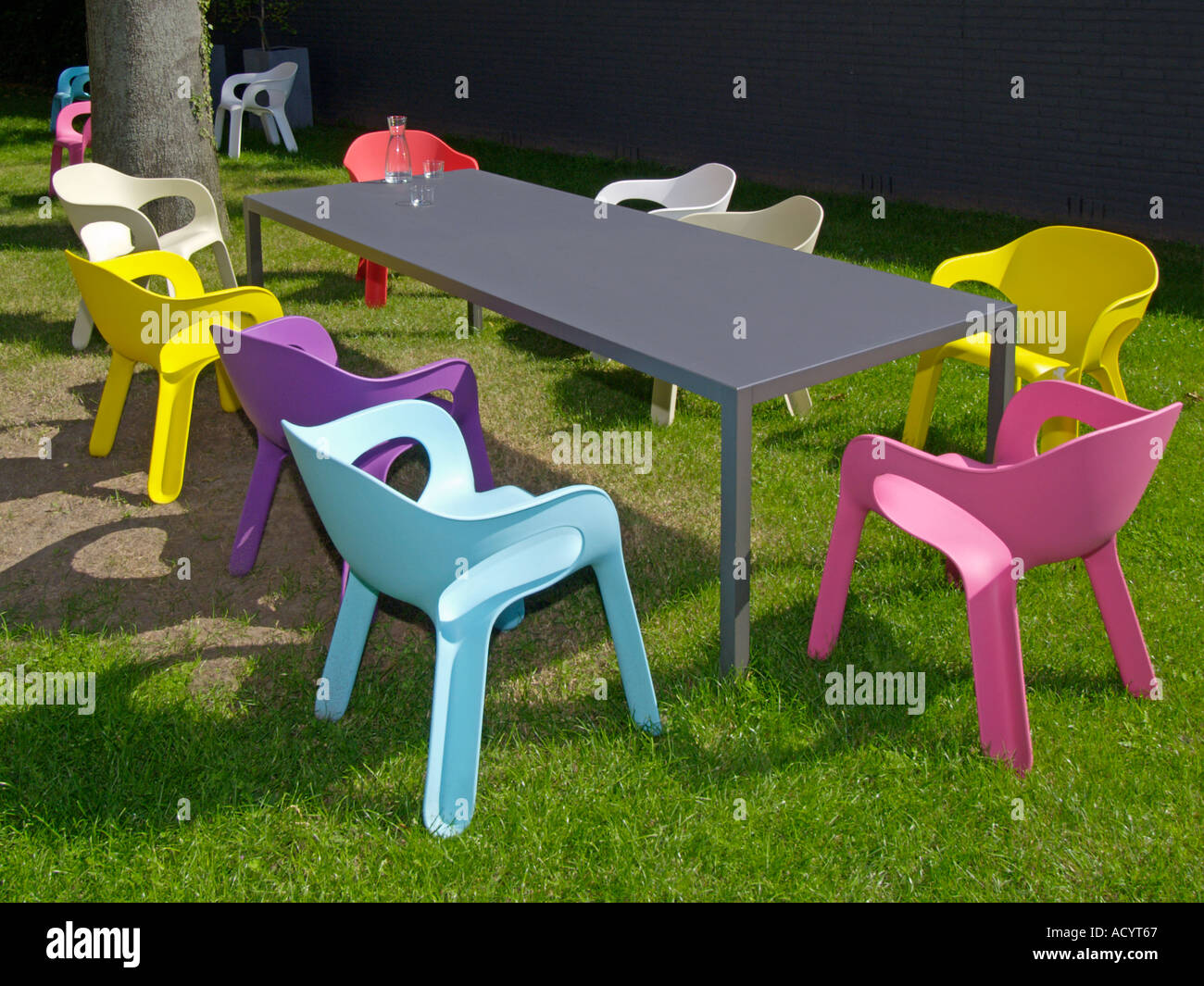 Molti vivacemente colorato in plastica Sedie design intorno al grande tavolo  grigio nel giardino soleggiato Foto stock - Alamy