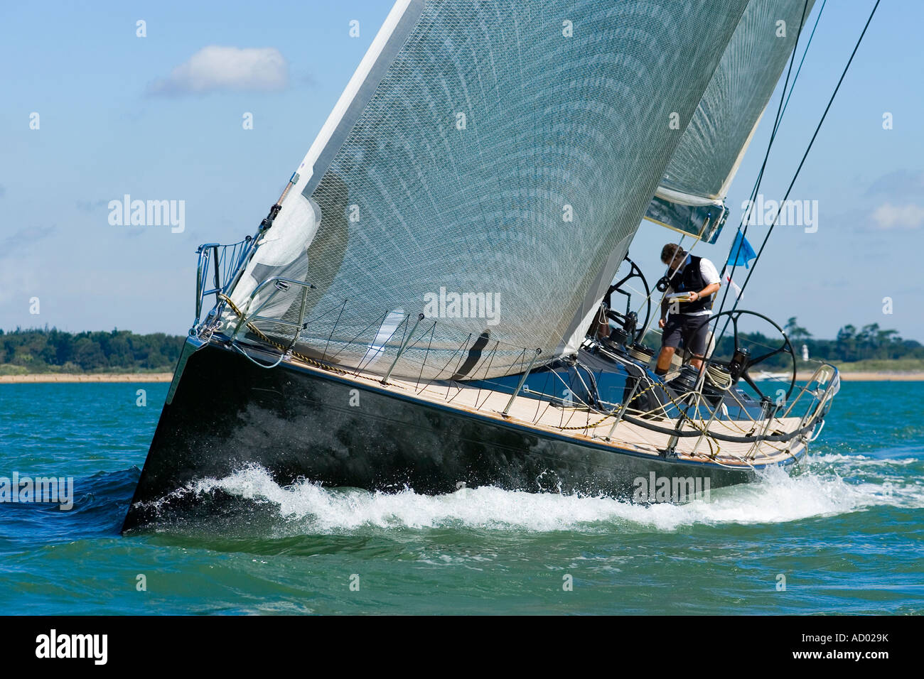 Un potente black racing yacht con vento vele pieni poteri attraverso acque costiere Foto Stock