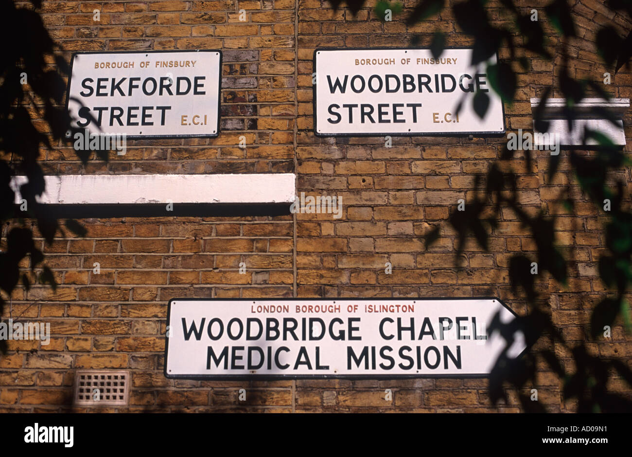 London street segni e direzione di Woodbridge cappella missione medica giallo su un muro di mattoni, Clerkenwell, Londra, Inghilterra Foto Stock