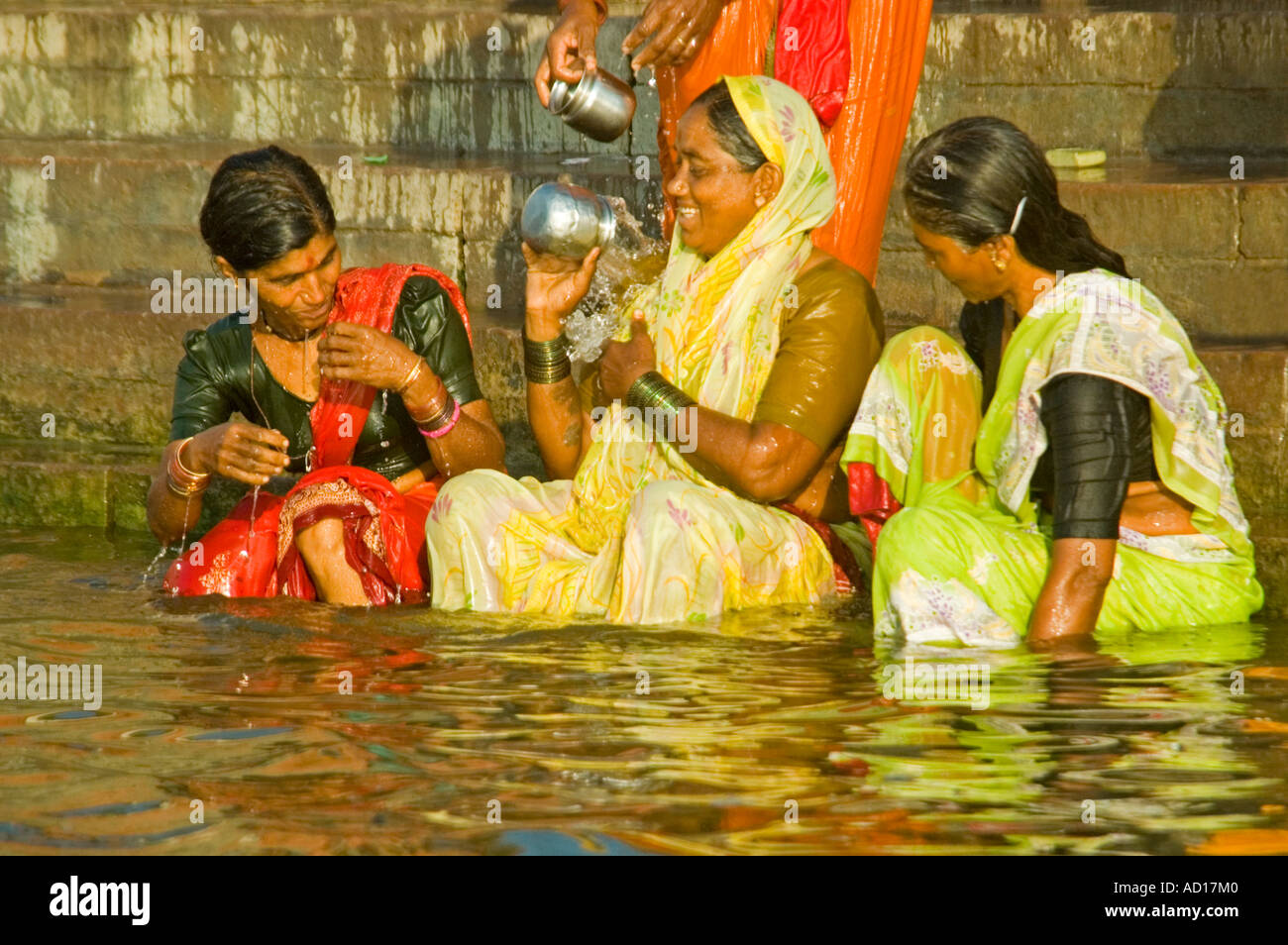 Chiudere orizzontale di tre sorridere le donne indiane lavaggio su Ahilyabai Ghat semi sommerse nell'acqua nelle prime ore del mattino sun Foto Stock