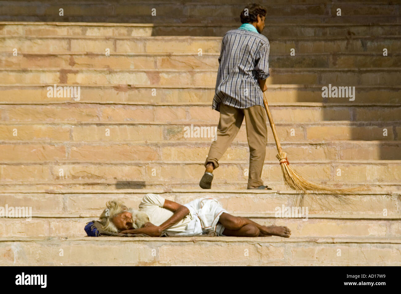 Chiudere orizzontale di una disperatamente poveri sottile vecchio uomo dorme roungh sui gradini con un uomo spazzare fino intorno a lui. Foto Stock