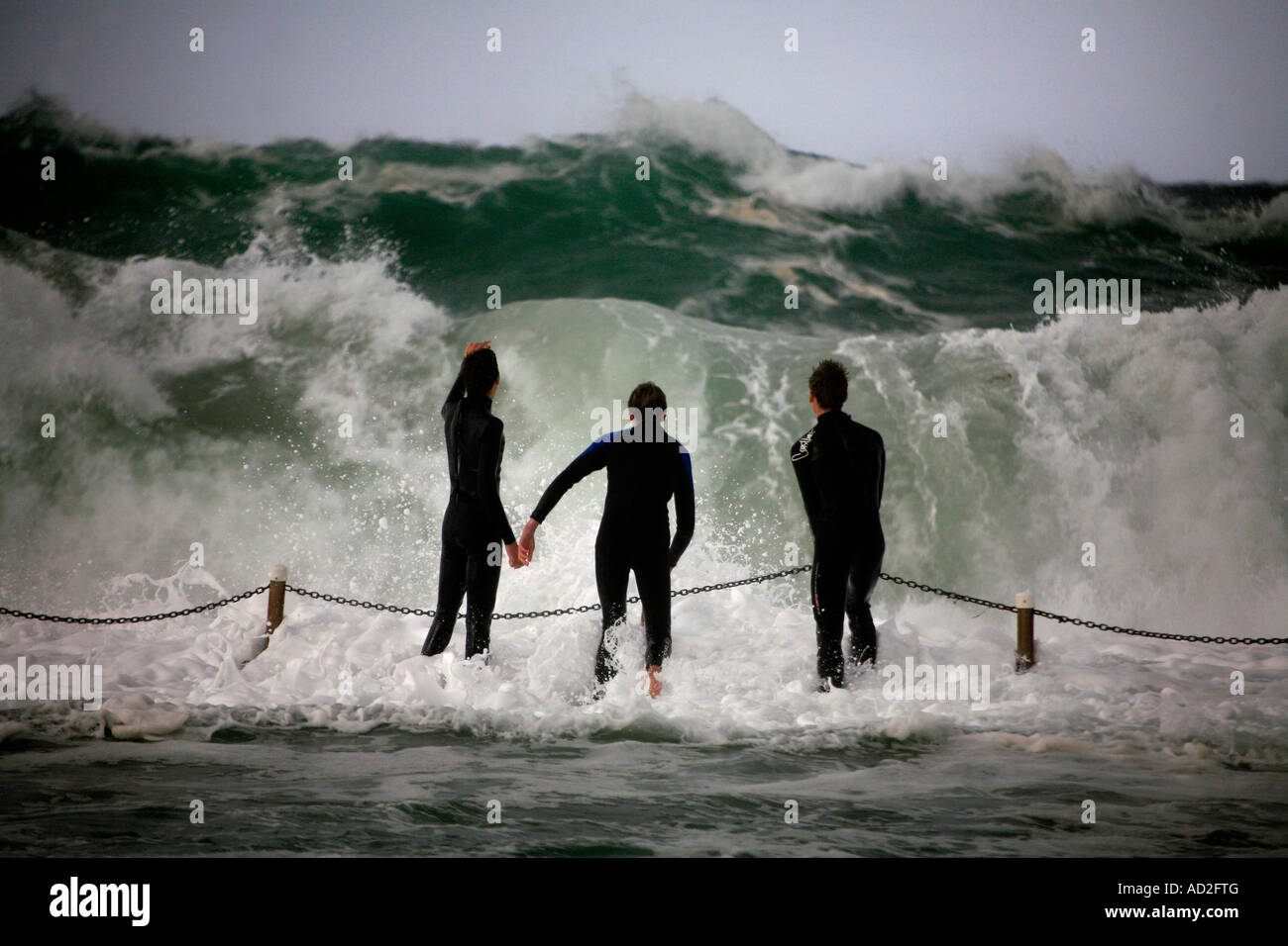 Giovani ragazzi adolescenti taunt sorte in piedi nel percorso del grande oceano onde durante una tempesta ciclonica a Dee Why Sydney Australia Foto Stock