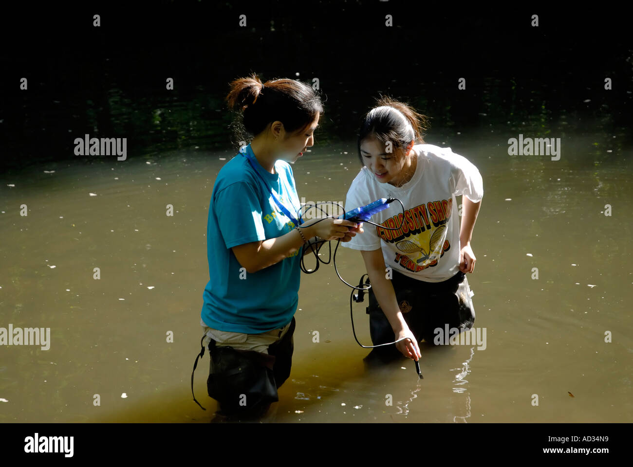 Teenage Asiatico-americano di ragazze di campionamento di acqua di fiume con digital per ossigeno disciolto come indicatore chimico della qualità dell'acqua Foto Stock