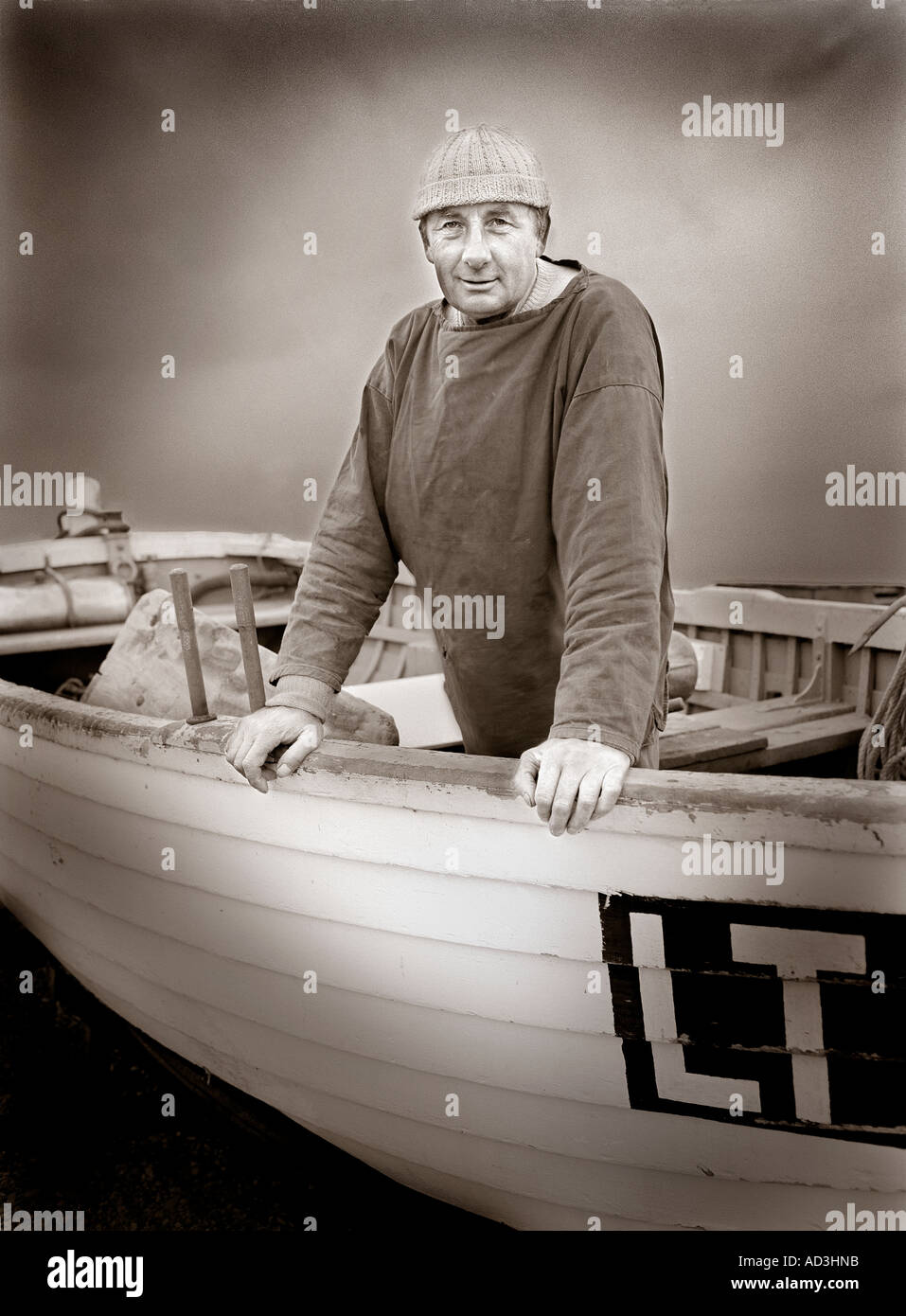 Ritratto di deep sea fisherman in posa il suo vecchio legno barca da pesca a Dunwich nel Suffolk, Inghilterra, Regno Unito Foto Stock