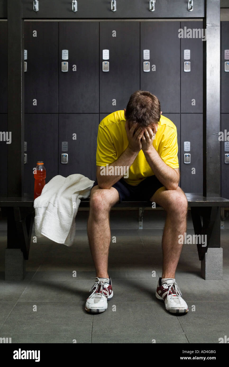 Un uomo seduto con la testa tra le mani in un Locker room Foto Stock