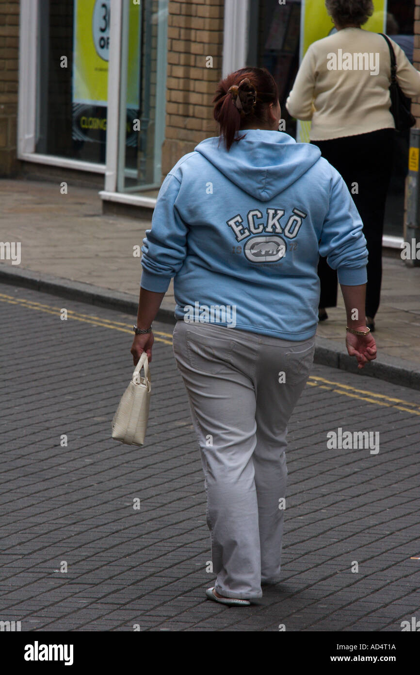 Vista posteriore di una donna obesa camminare portando un sacchetto Foto Stock
