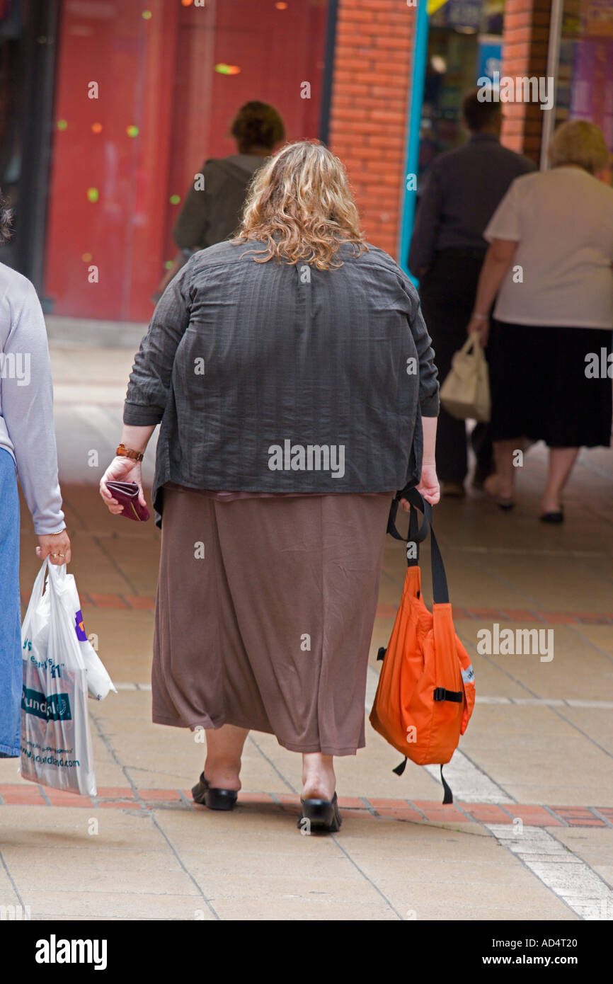 Vista posteriore di una donna obesa camminare portando un sacchetto Foto Stock