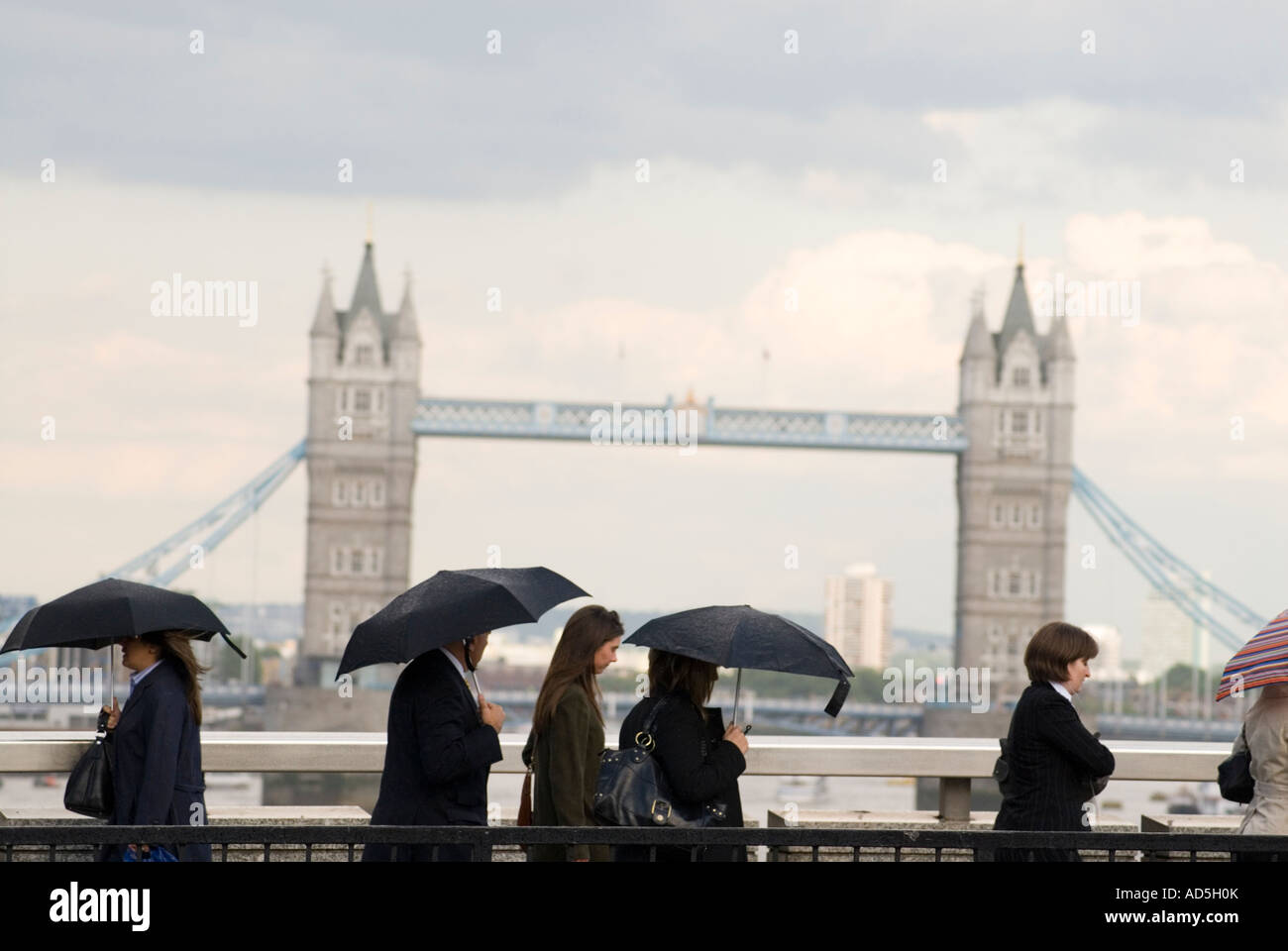 Pendolari sotto la pioggia a camminare lungo il Tower Bridge di Londra Inghilterra REGNO UNITO Foto Stock