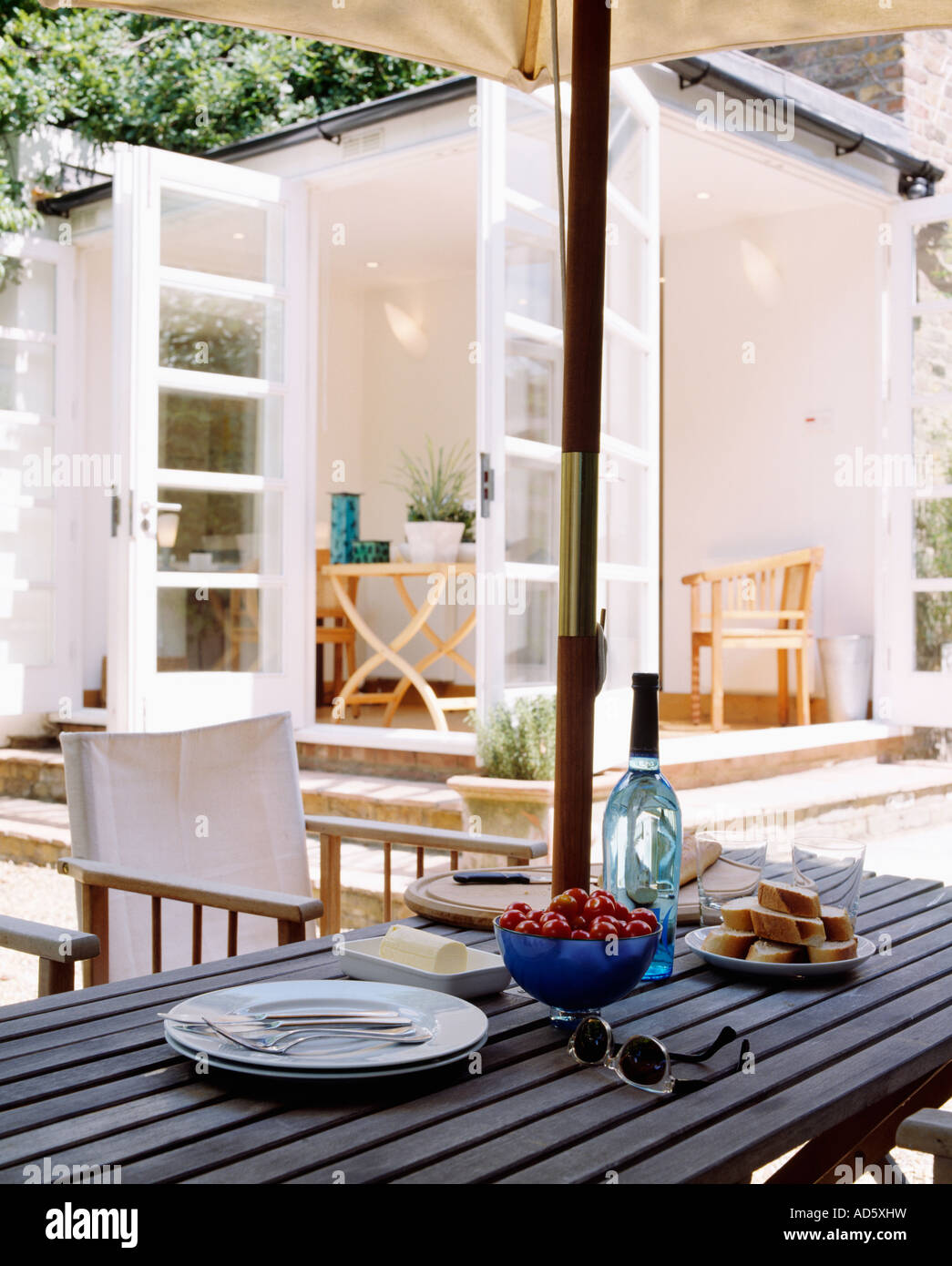 Piastre e cibo sul patio in legno tavolo con direttore bianco s sedie e  ombrellone e vista di bianca e moderna estensione livingroom Foto stock -  Alamy