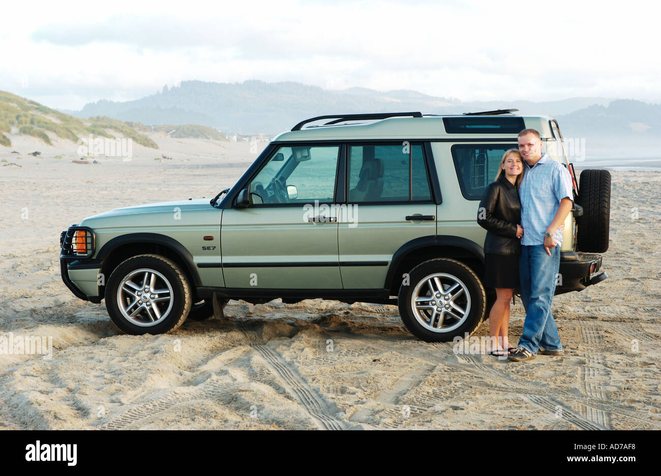 Coppia giovane permanente sulla spiaggia di fronte di SUV Foto Stock